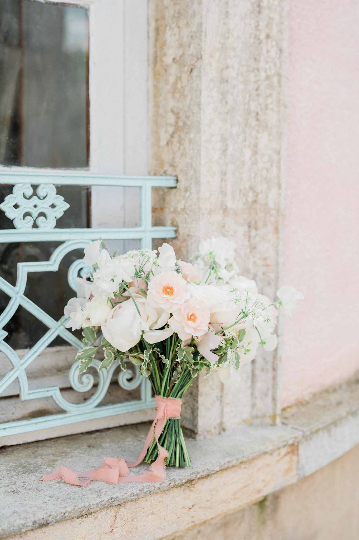 Bridal bouquet with ivory and blush roses against pale stone building with blue shutters