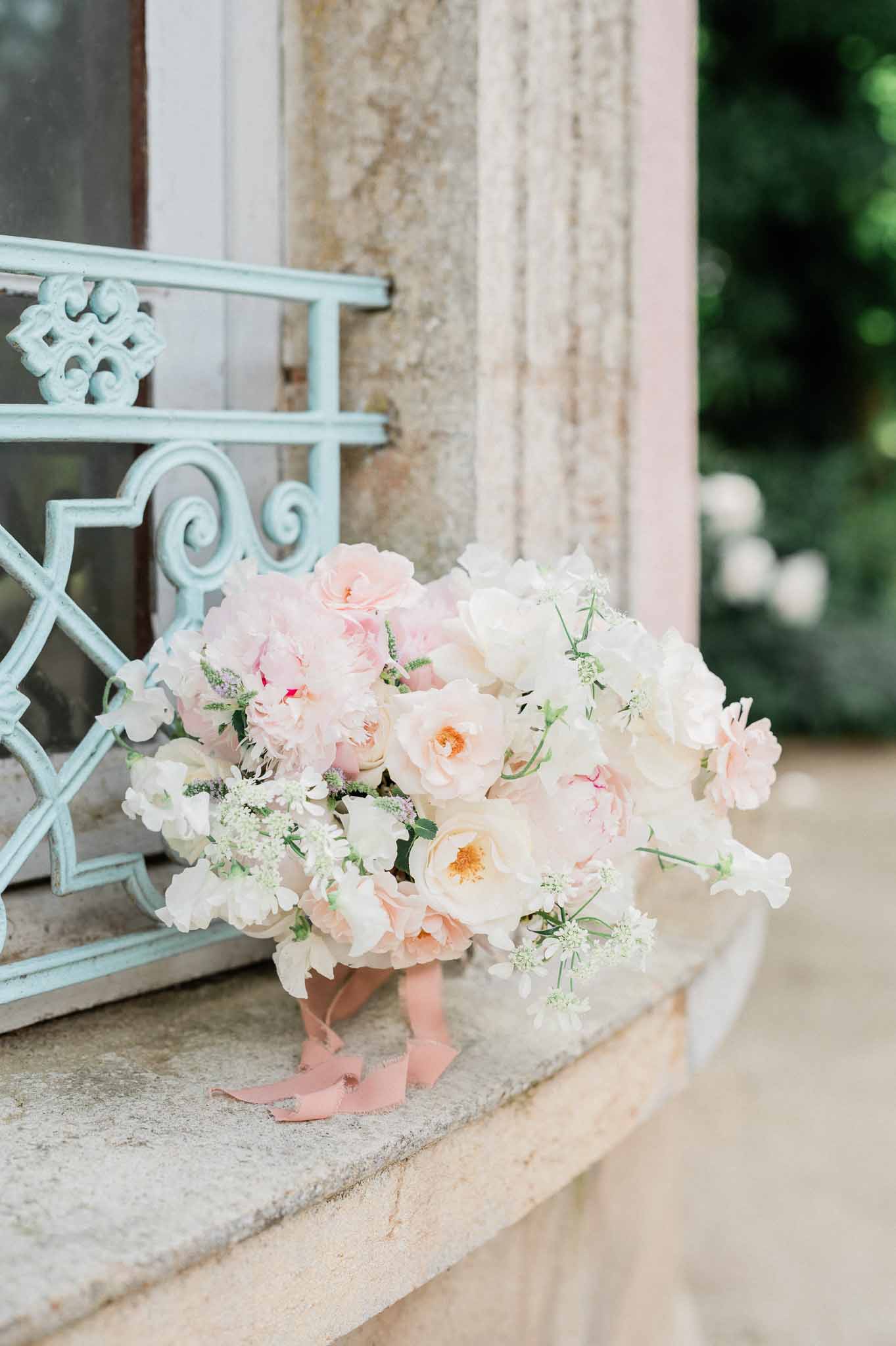 Bridal bouquet with pink roses and peonies on stone ledge at garden venue