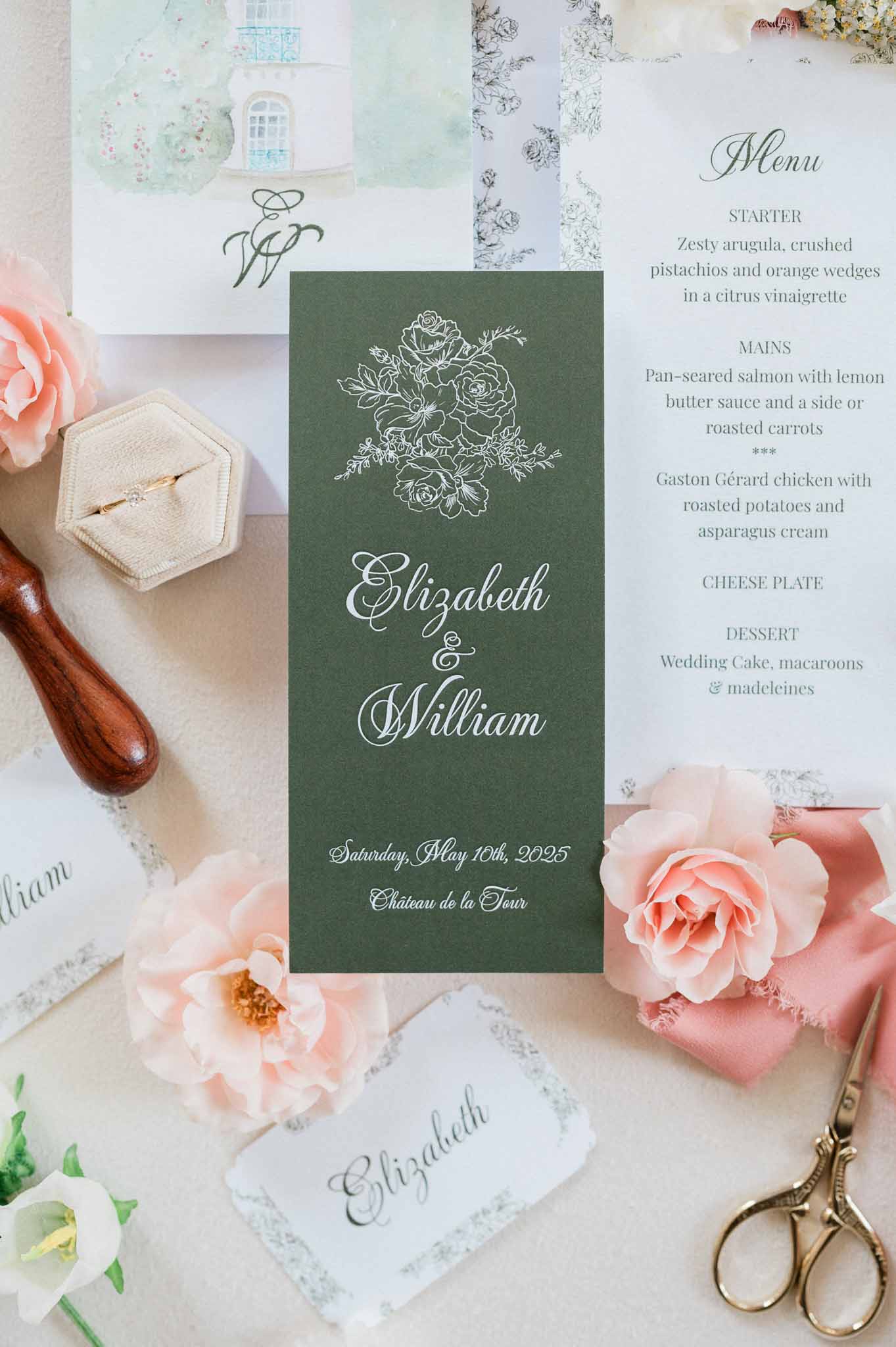 Wedding stationery flat lay with forest green menus, roses, and rings at Chateau de la Tour
