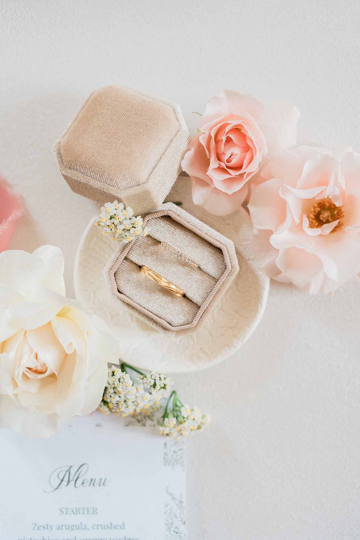 Gold wedding bands in linen box with blush roses and menu card flat lay styling