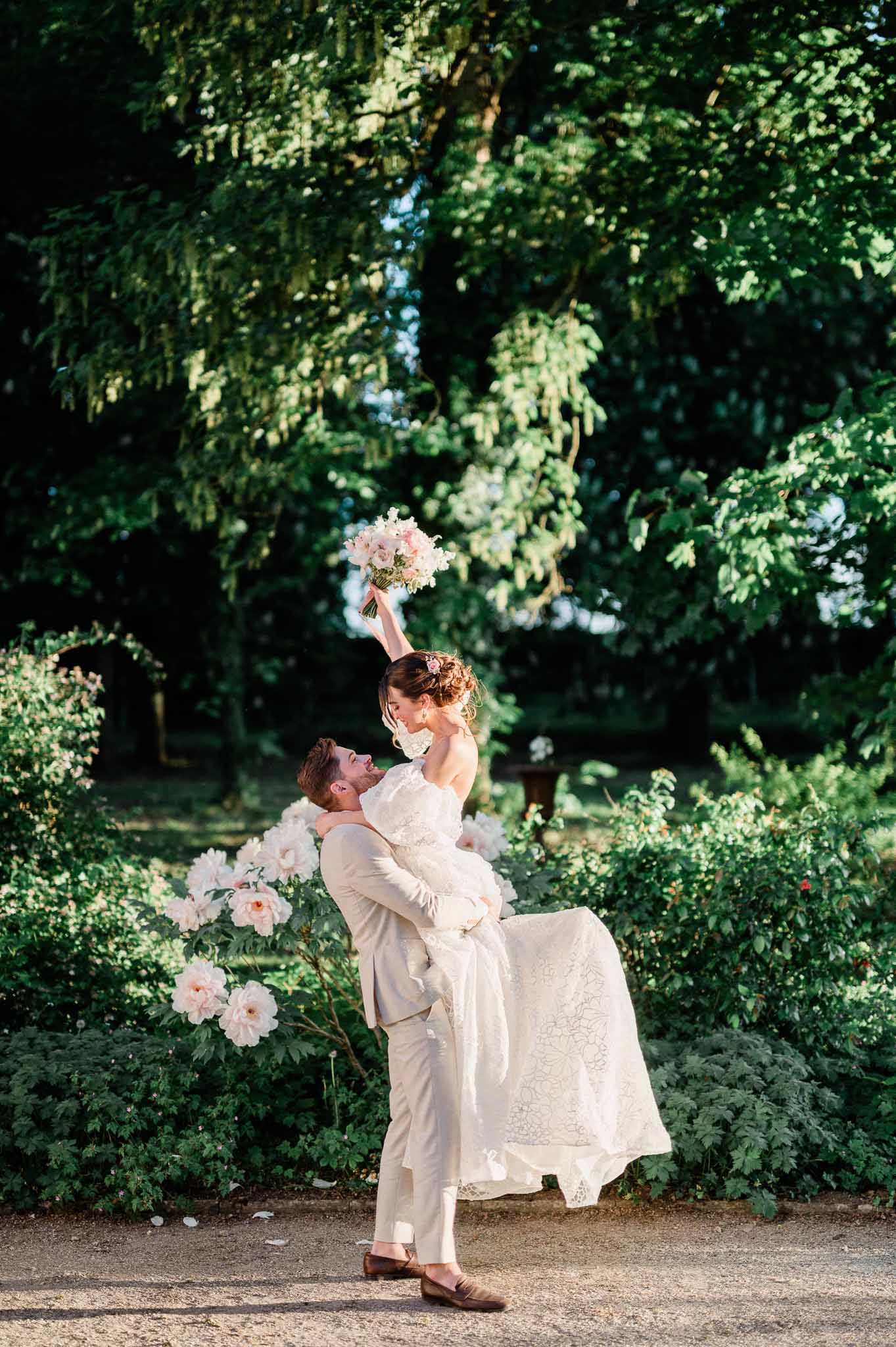 Groom lifting bride in playful portrait moment in garden setting with climbing roses