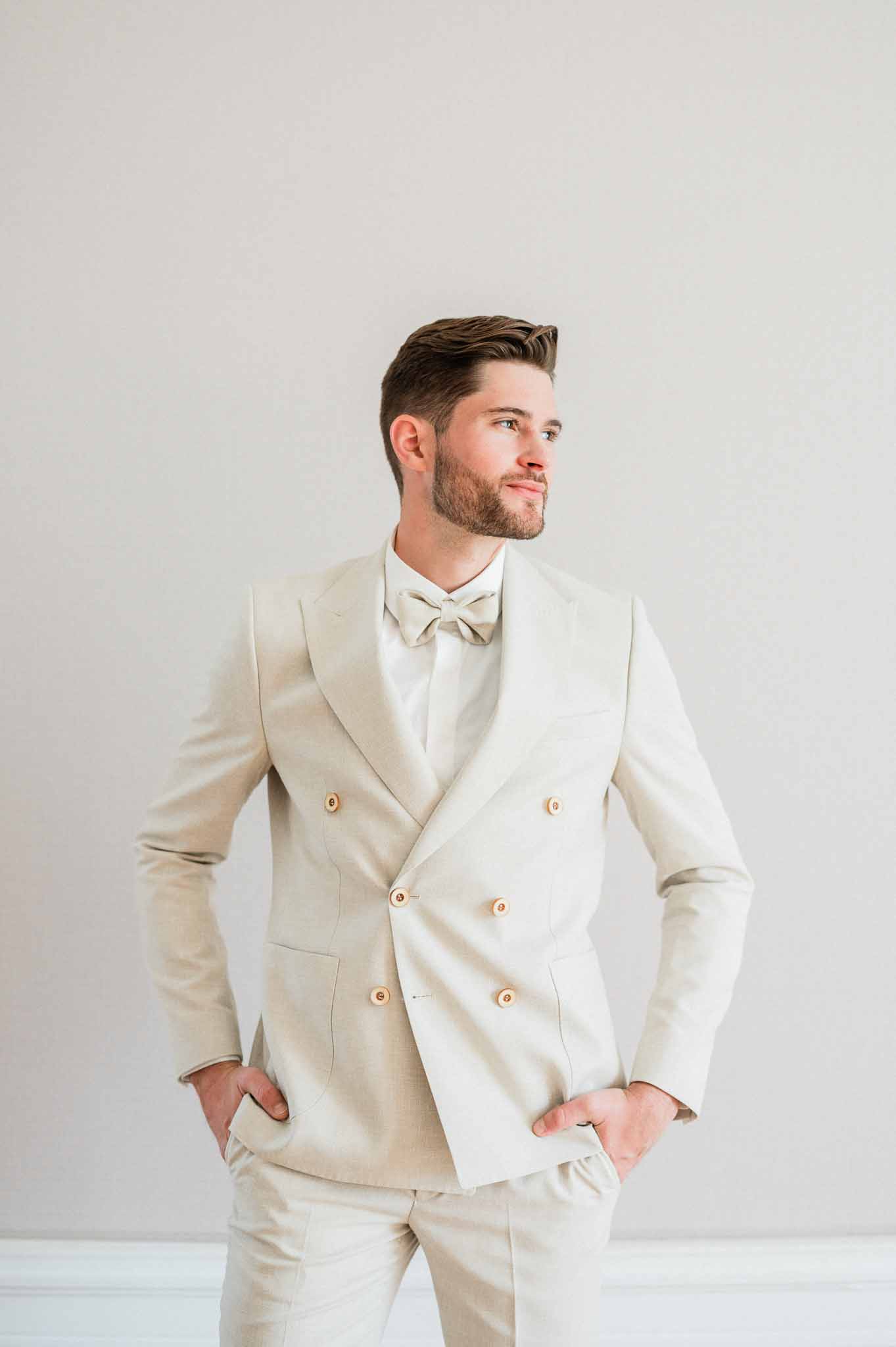 Groom in cream double-breasted suit with rose gold buttons studio portrait