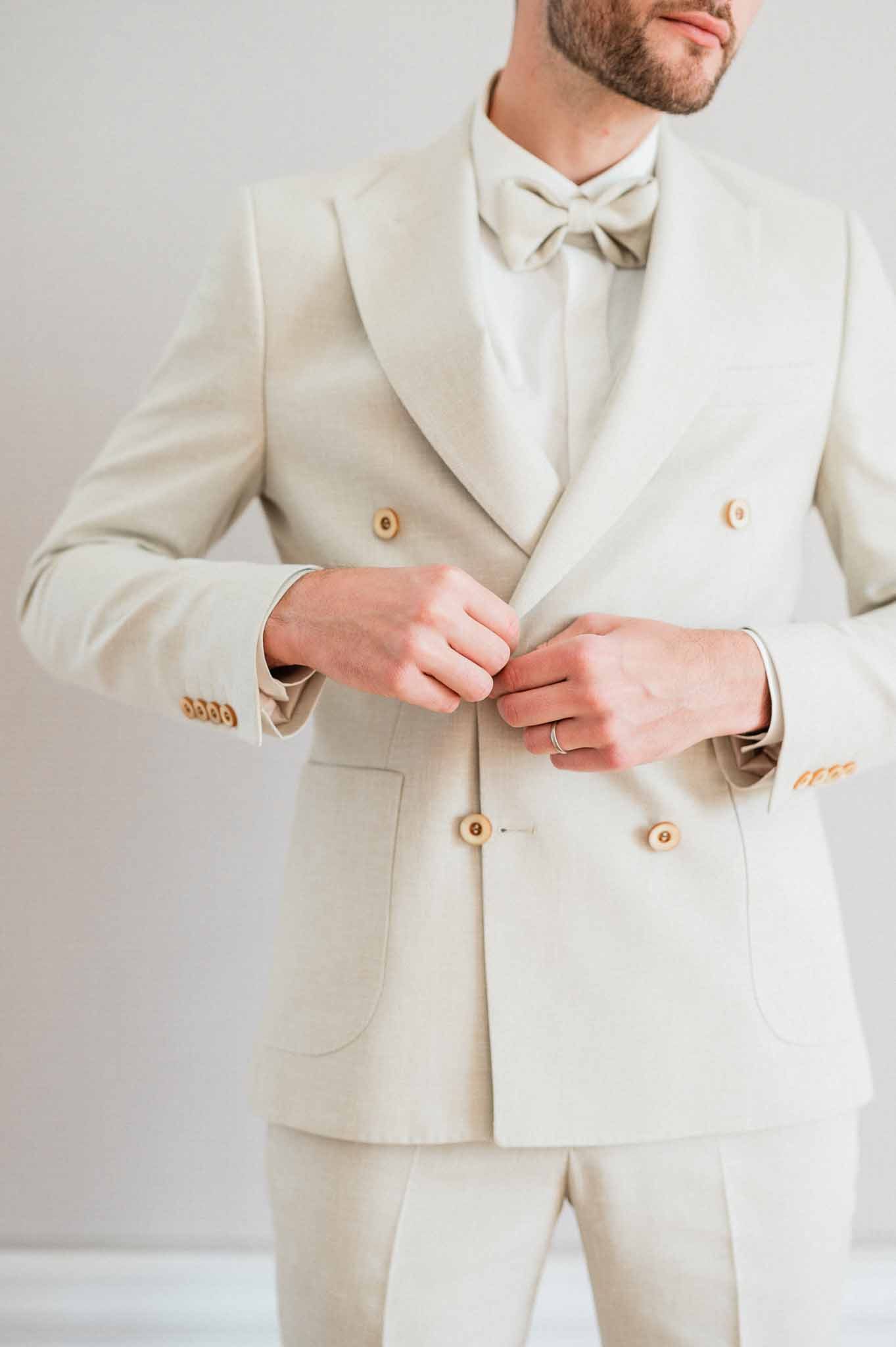 Groom adjusting cream suit jacket during wedding preparation