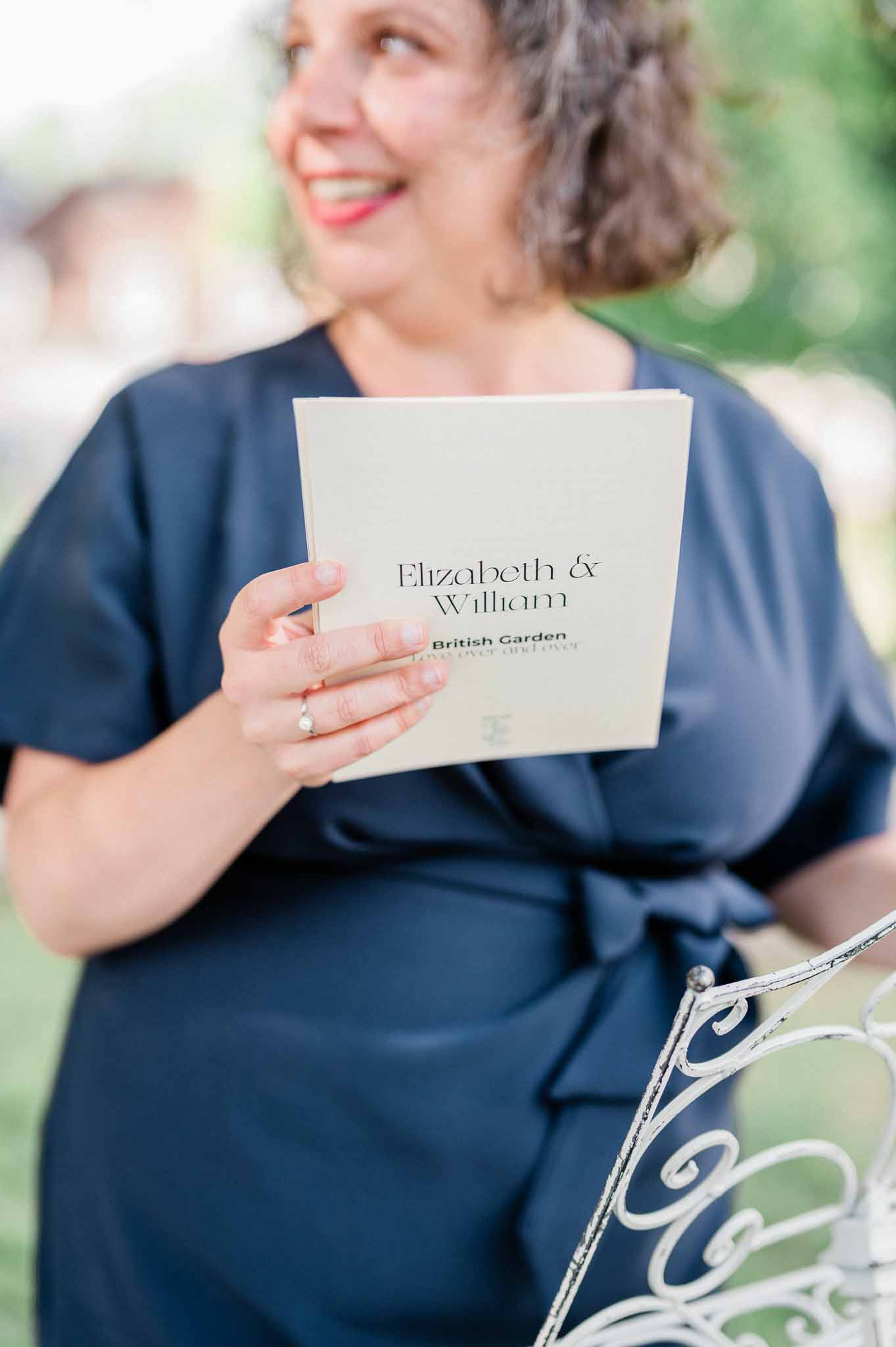 Wedding guest holding ivory program at outdoor garden wedding ceremony
