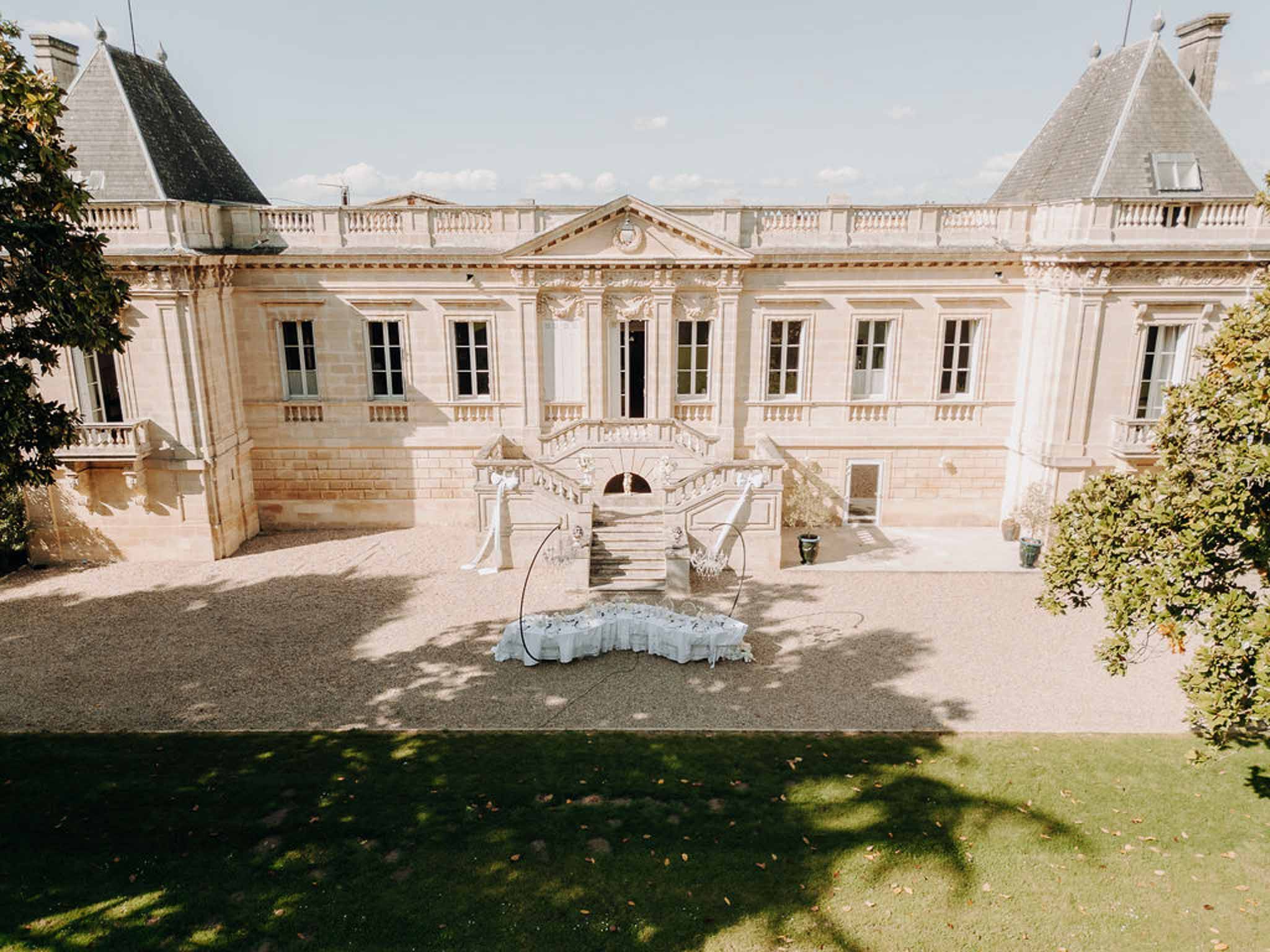 Aerial view of limestone chateau with twin towers white ceremony draping and circular arch on gravel courtyard