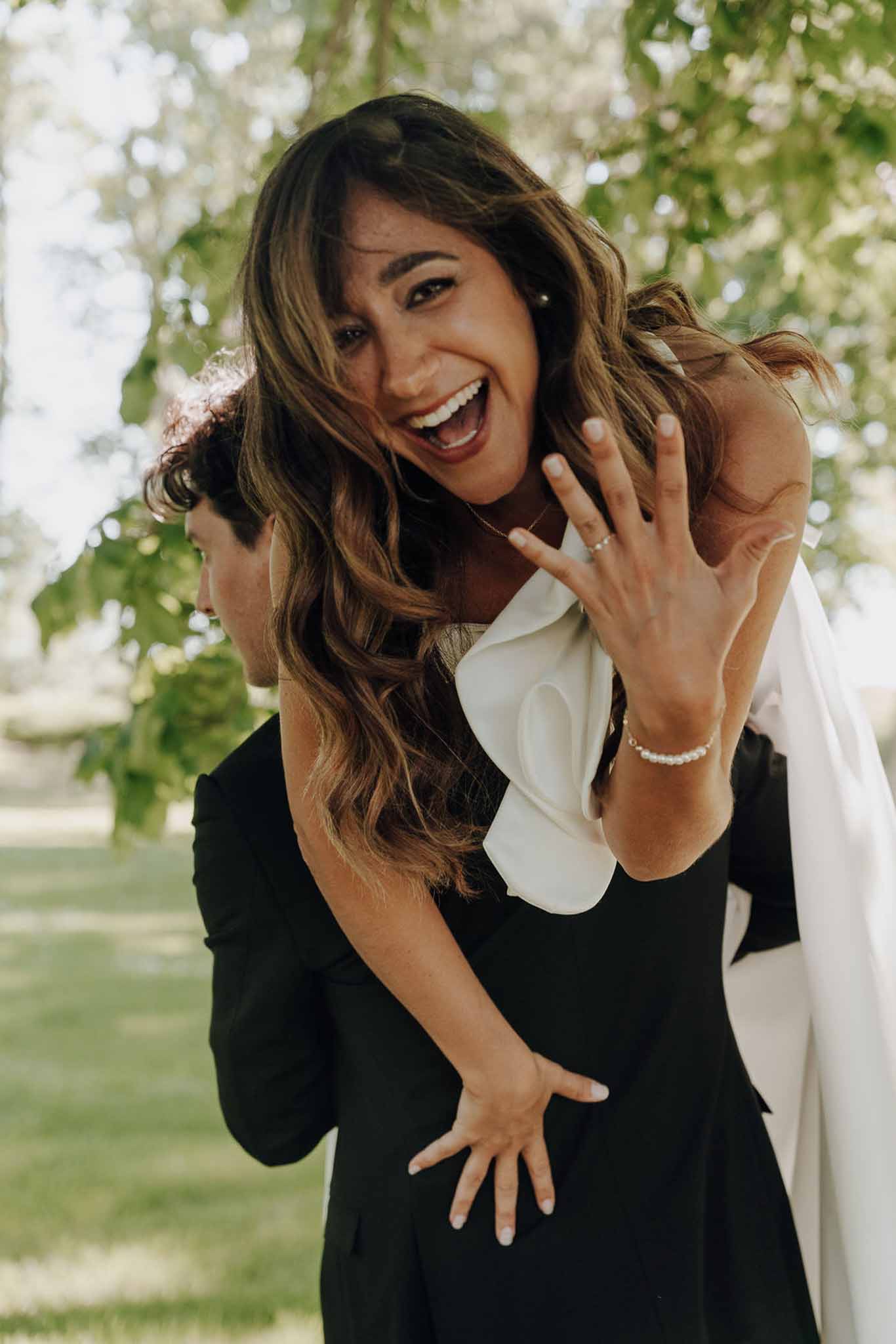Candid portrait of bride on groom's back showing wedding rings and tennis bracelet in garden setting