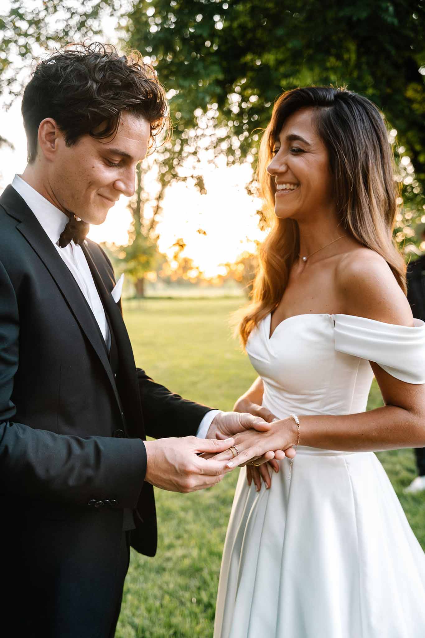 Groom placing wedding ring on bride's finger during golden-hour outdoor garden ceremony