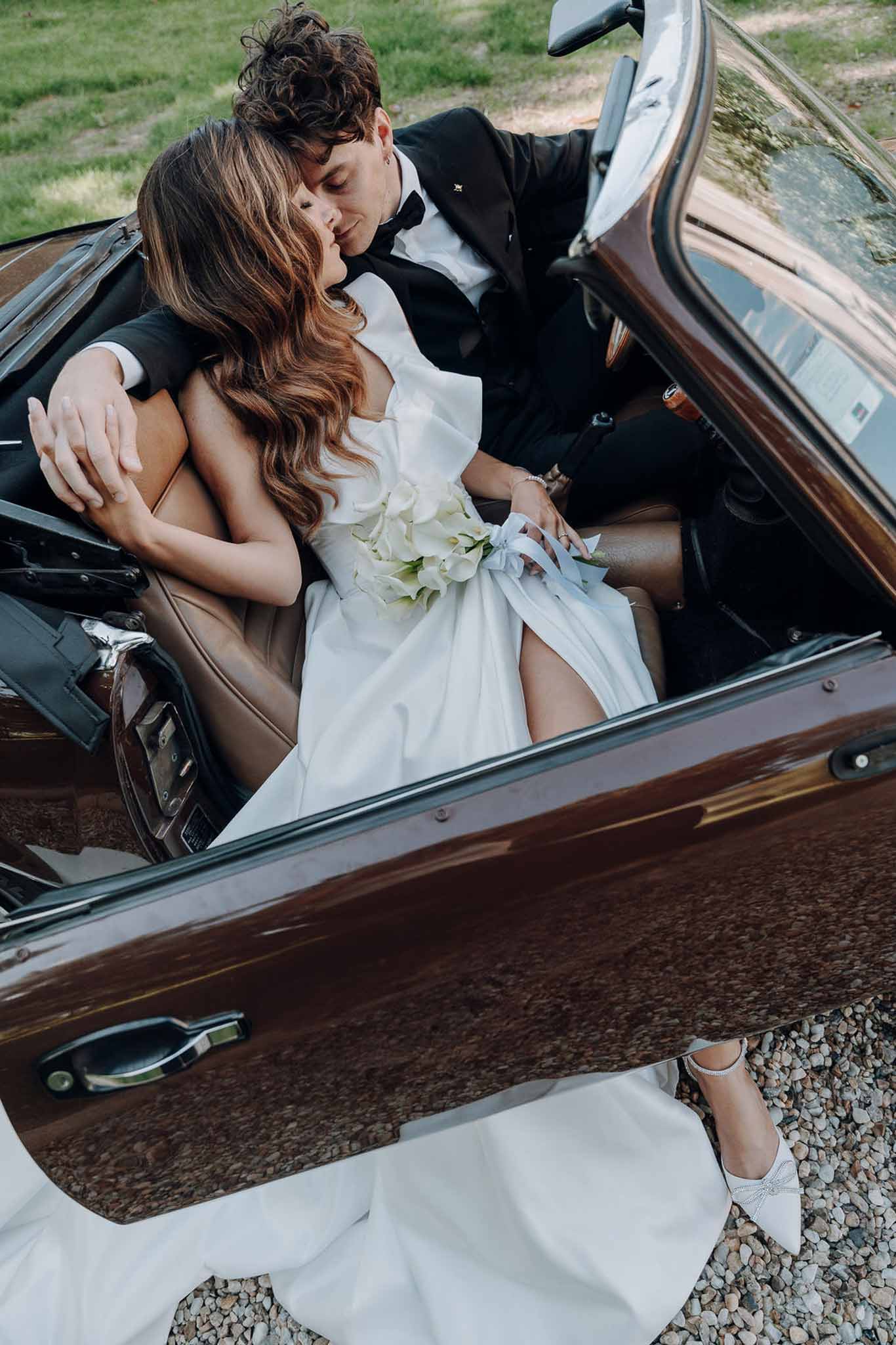 Overhead view of bride and groom kissing inside vintage brown convertible with calla lily bouquet
