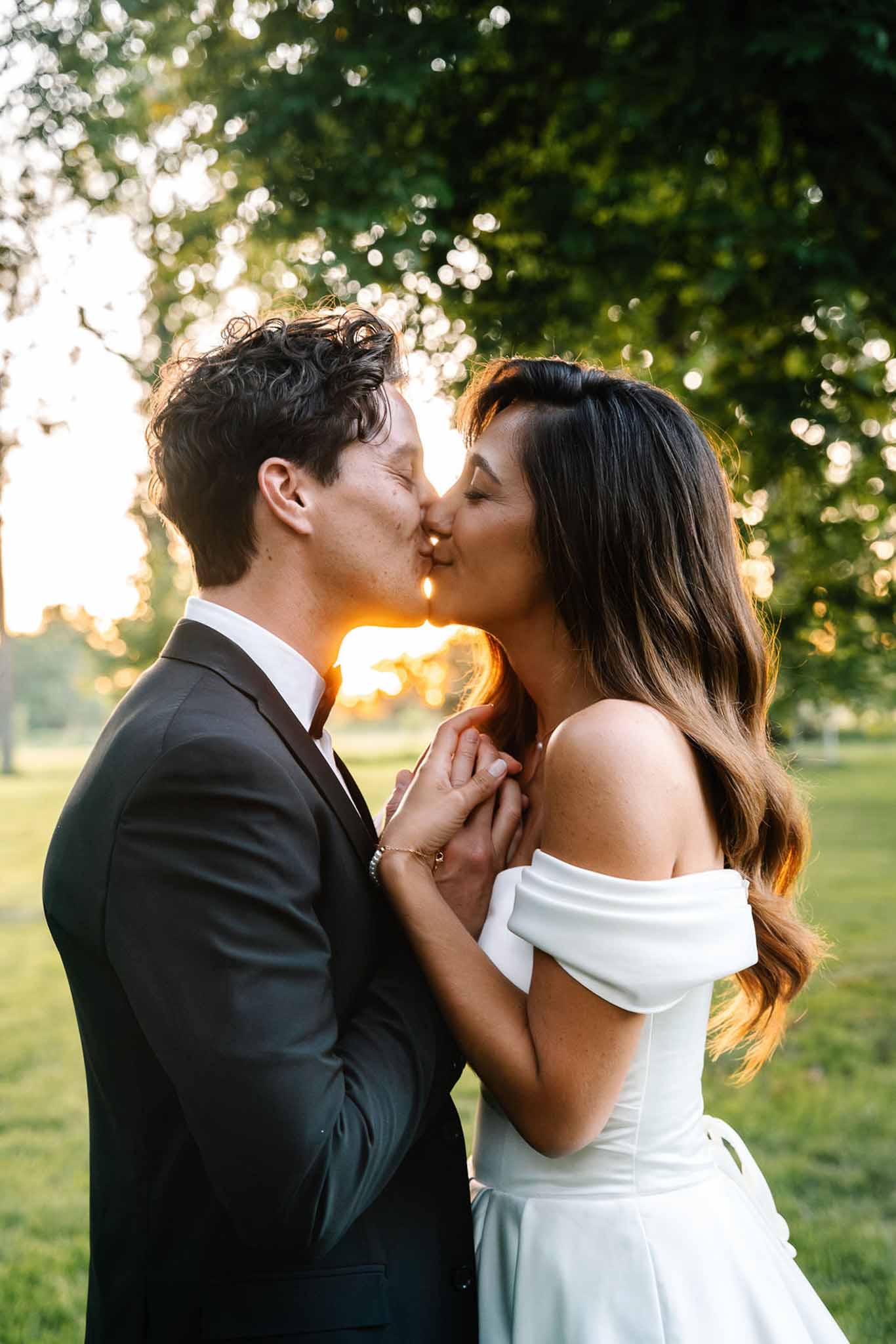 Bride and groom kissing during golden hour with warm backlight glowing between them outdoors