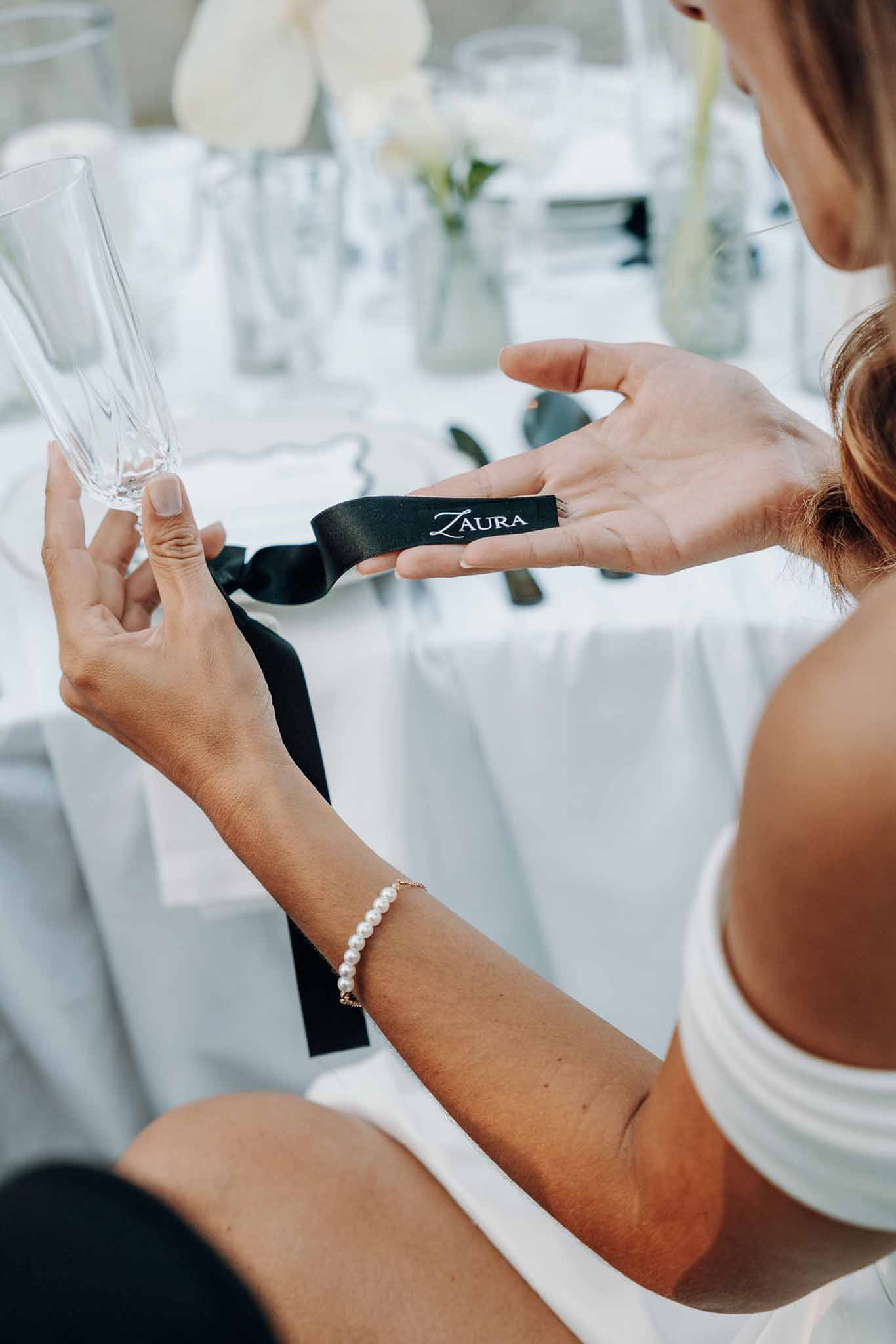 Close-up of hand holding champagne flute and black satin ribbon place card at white reception table