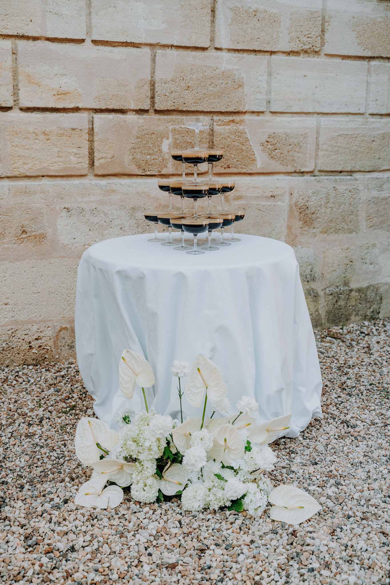 Champagne coupe glass tower on white-draped table with white anthurium and viburnum arrangement at base