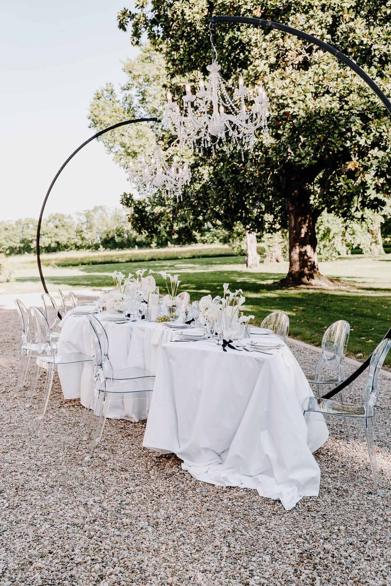Black and white themed reception table with calla lilies, ghost chairs, and suspended chandelier on arch