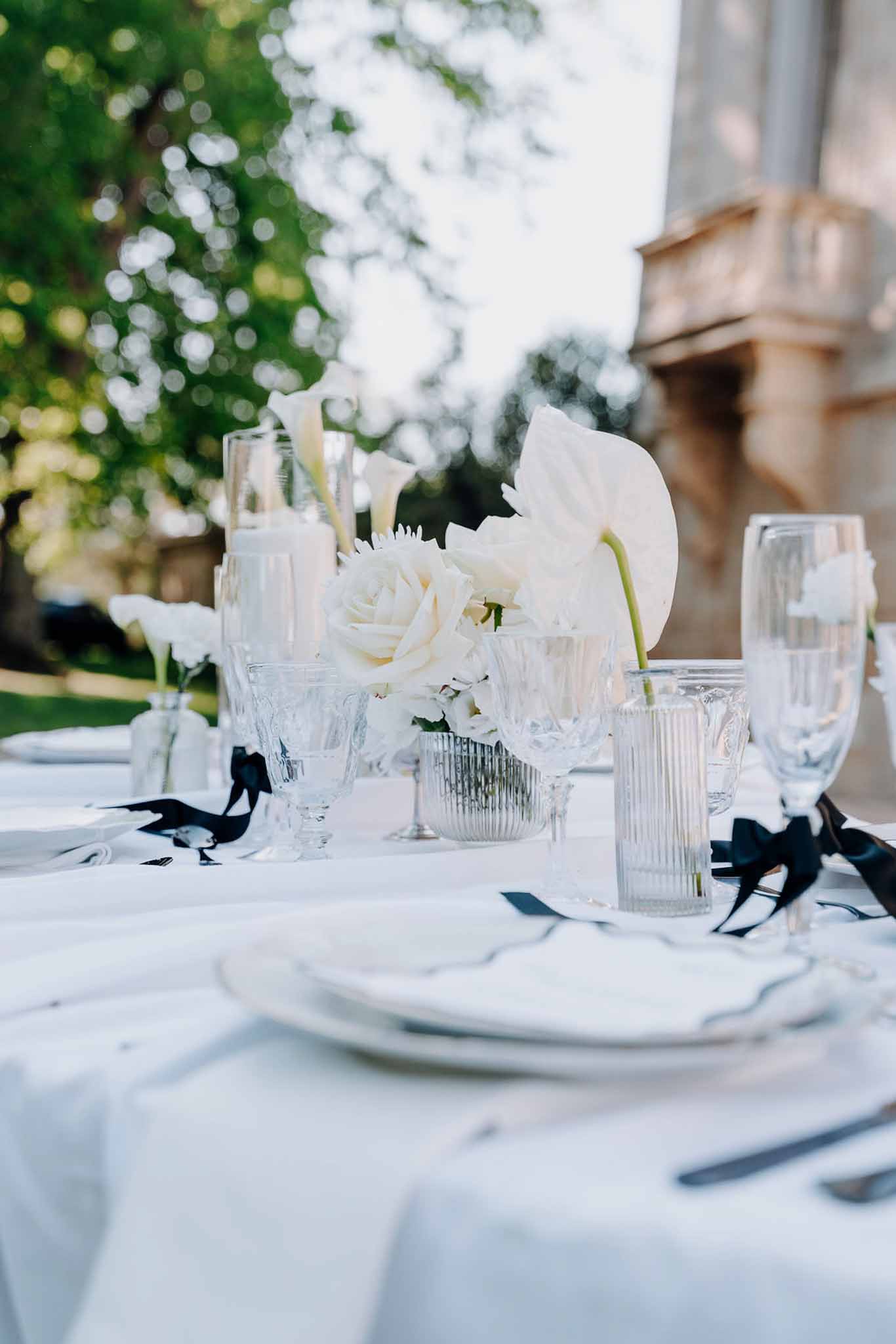 Monochromatic white table with anthurium calla lily bud vases and black ribbon napkin ties