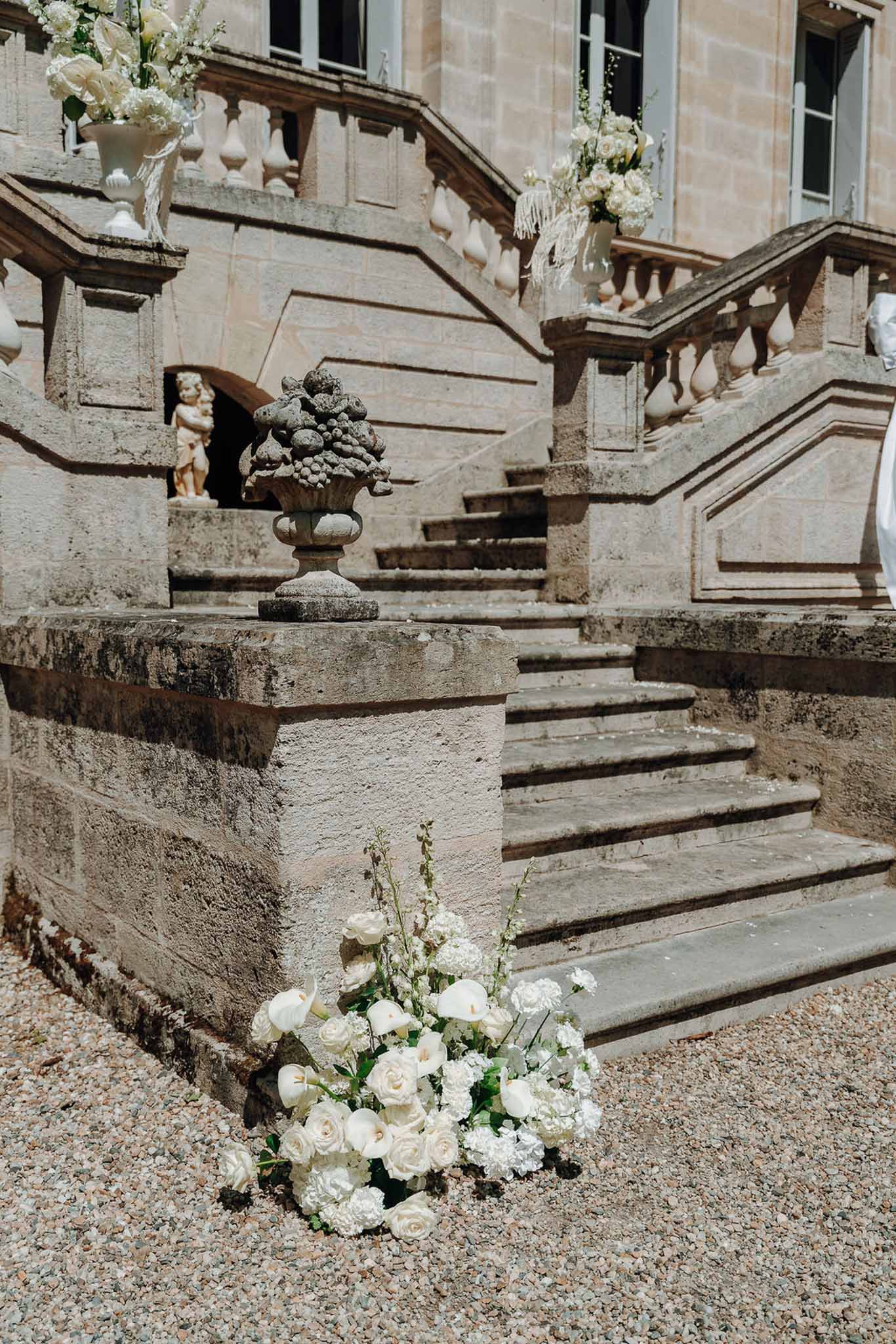 All-white floral arrangements of roses, calla lilies and hydrangea on chateau stone staircase entrance