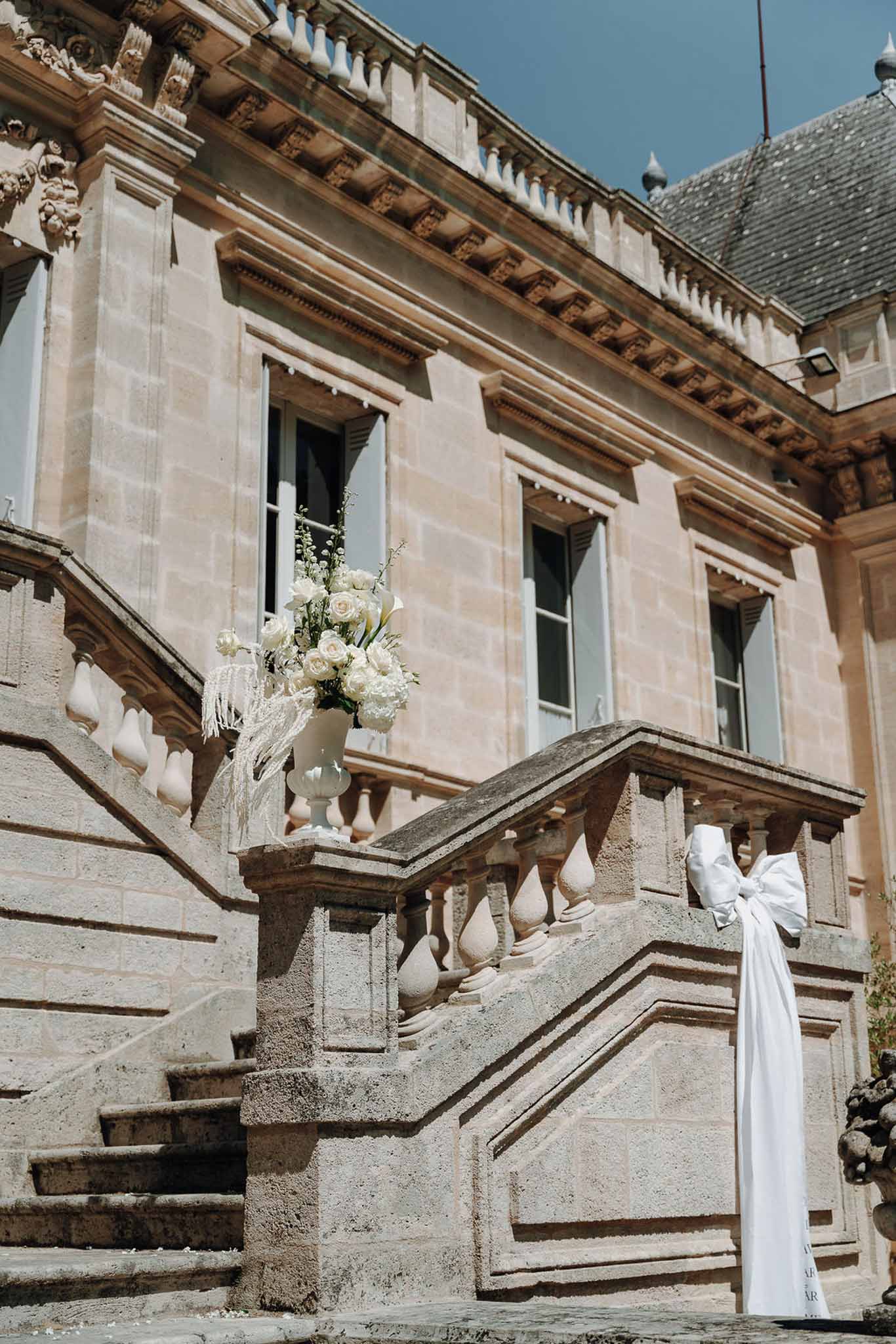Chateau stone staircase with ivory rose and calla lily urn arrangement and white satin bow on sandstone newel posts