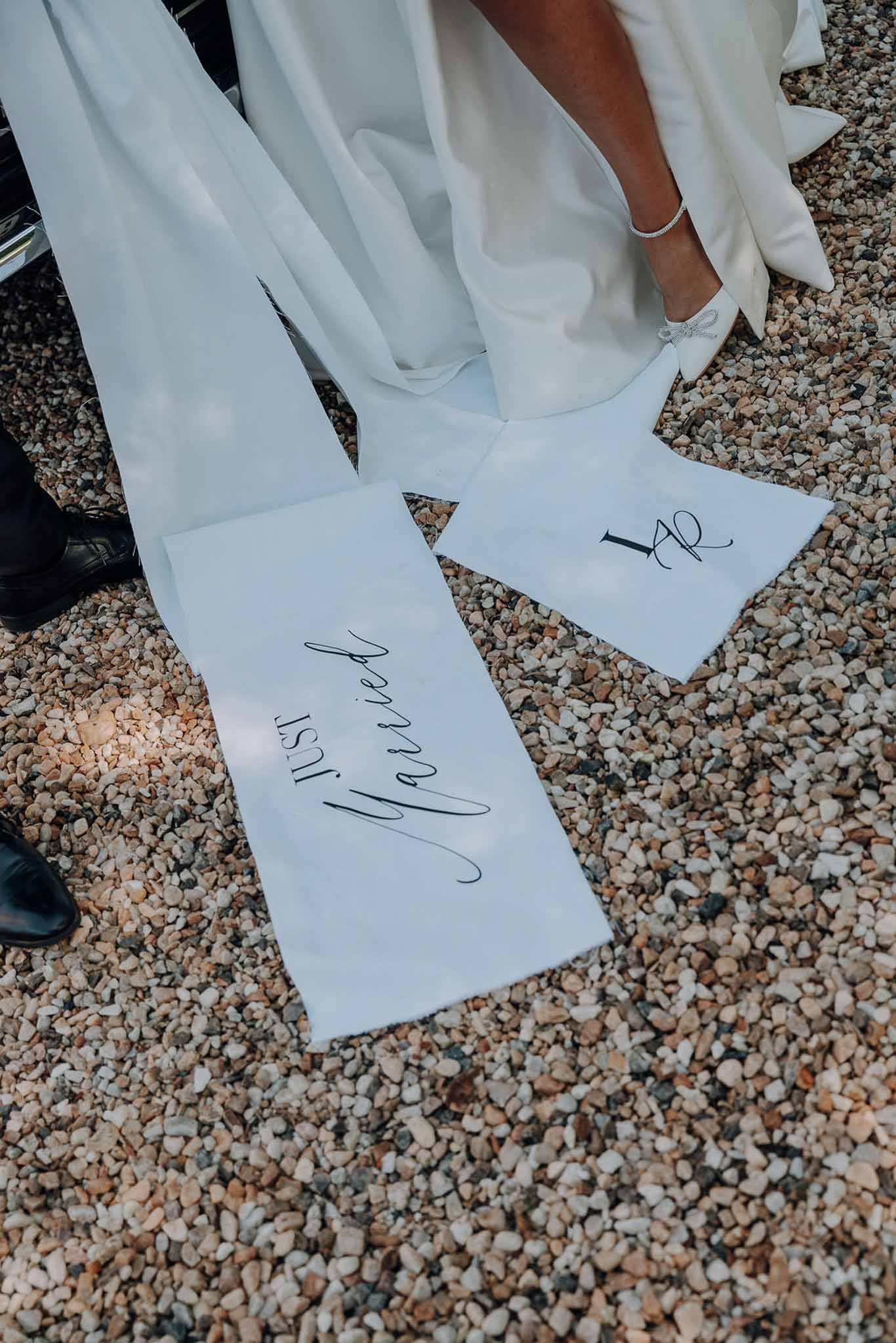 Close-up of personalised Just Married calligraphy on white satin dress train with crystal-strap heels