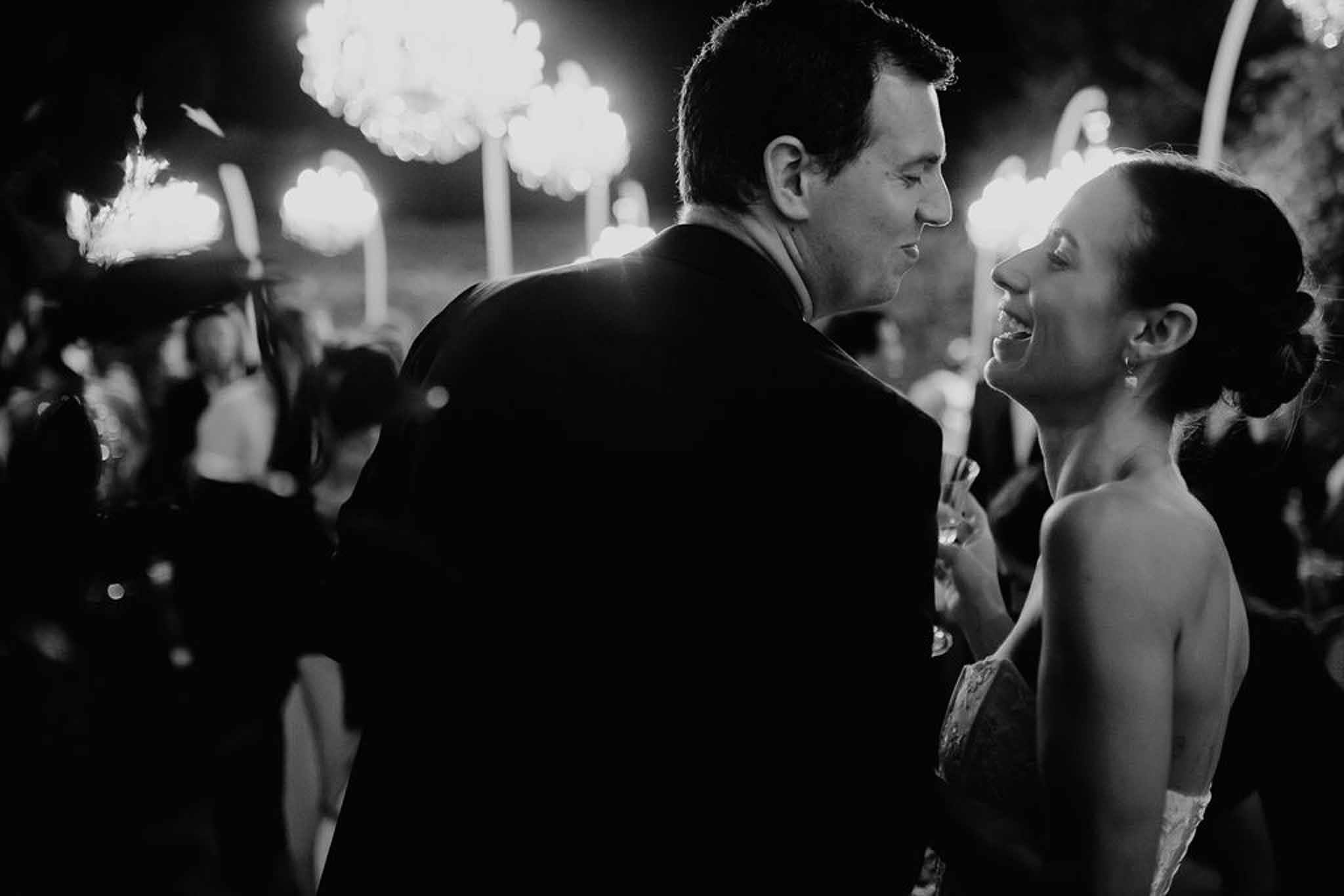 Bride laughing with groom during evening reception with chandelier bokeh in black and white