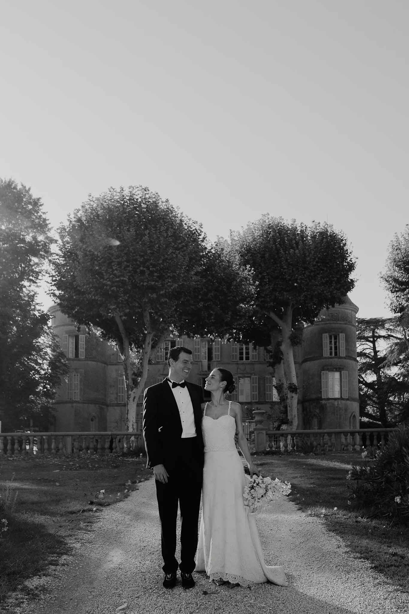 Black-and-white portrait of couple on chateau gravel driveway with turrets and mature trees behind