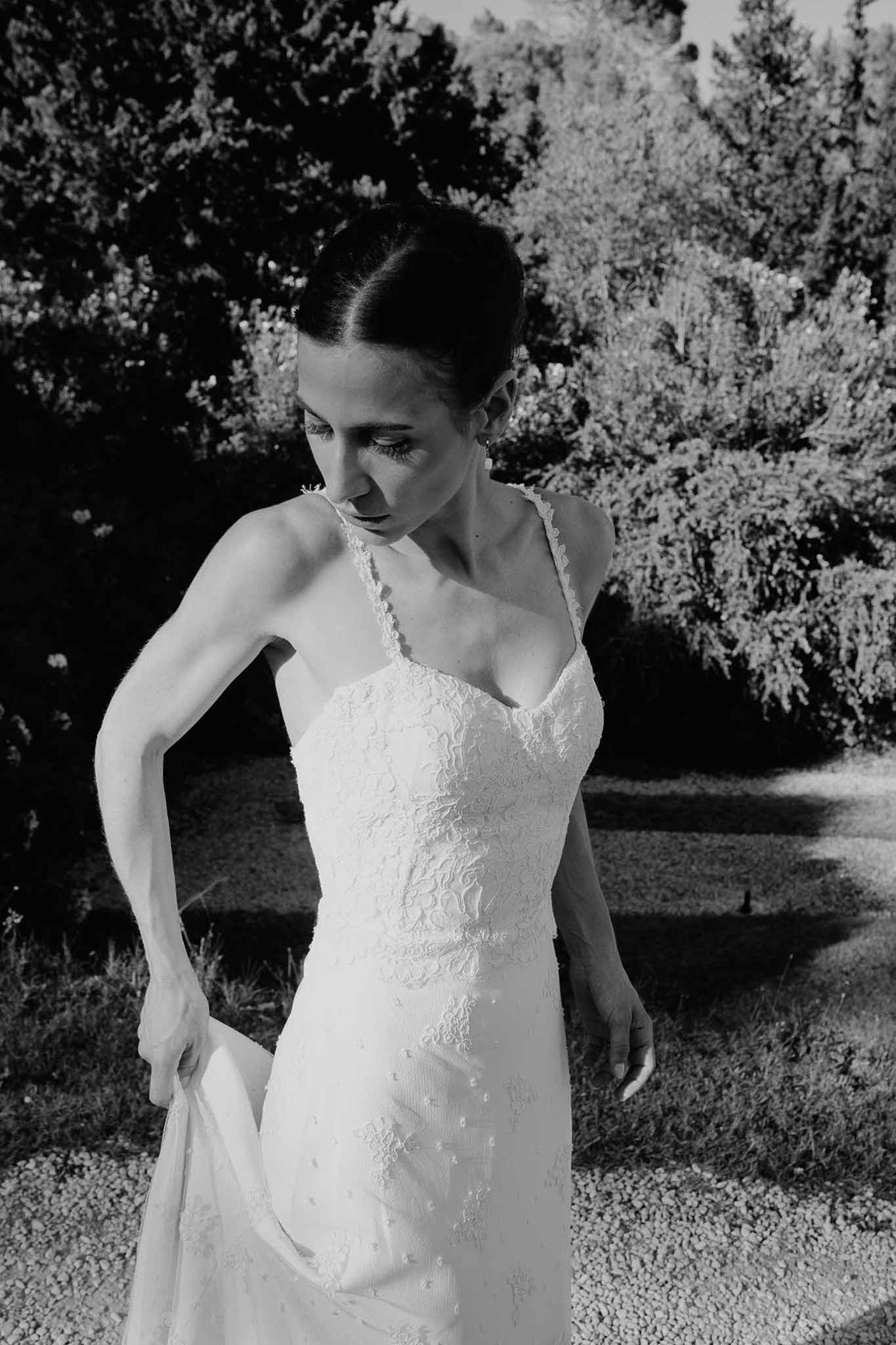 Black and white mid-length portrait of bride gathering lace gown skirt with updo and drop earrings