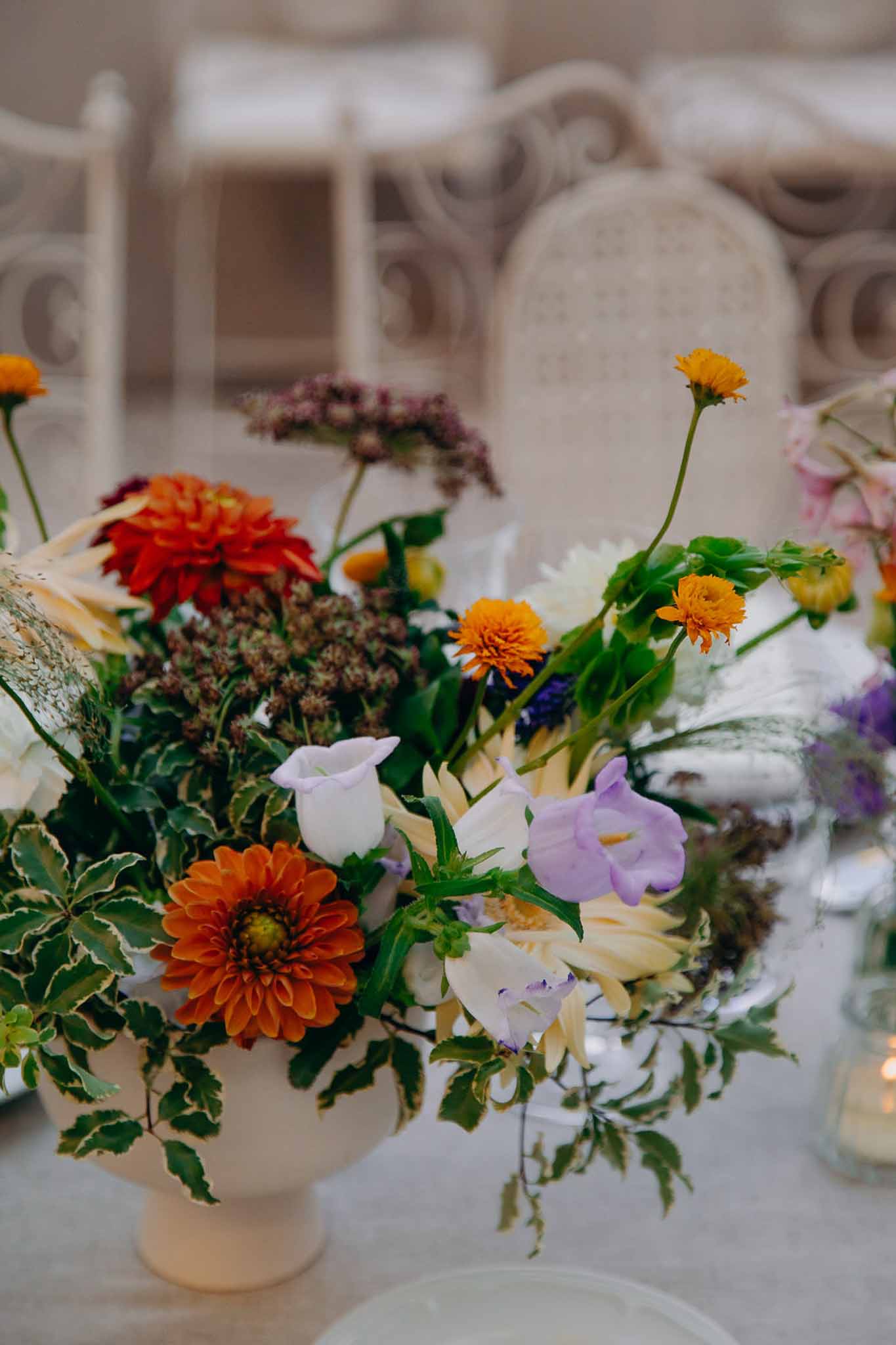 Vibrant centerpiece with orange dahlias, yellow marigolds, lavender sweet peas, and dried pampas grass
