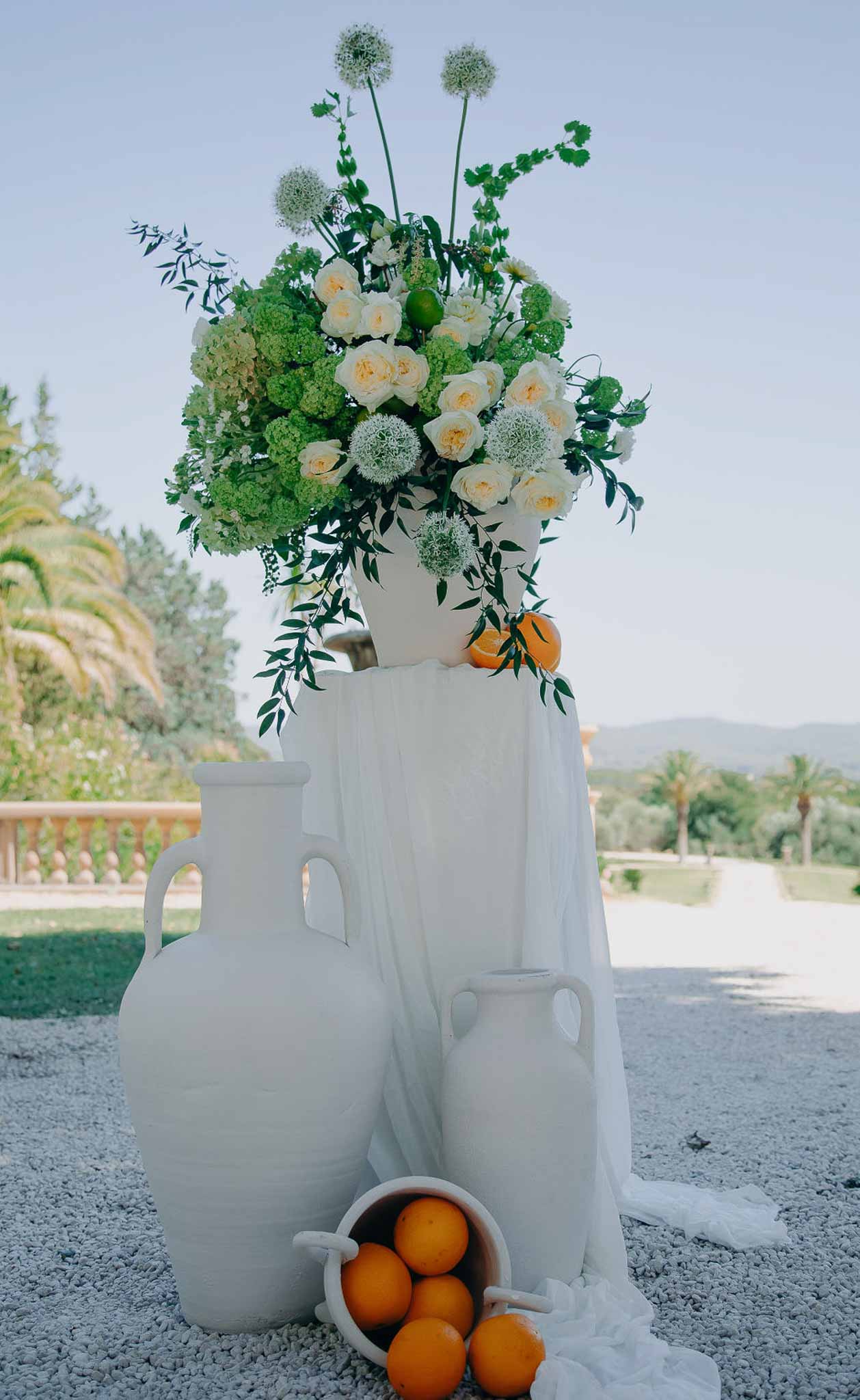 Mediterranean decor with white amphora jugs oranges and urn of cream roses green hydrangeas allium and olive foliage