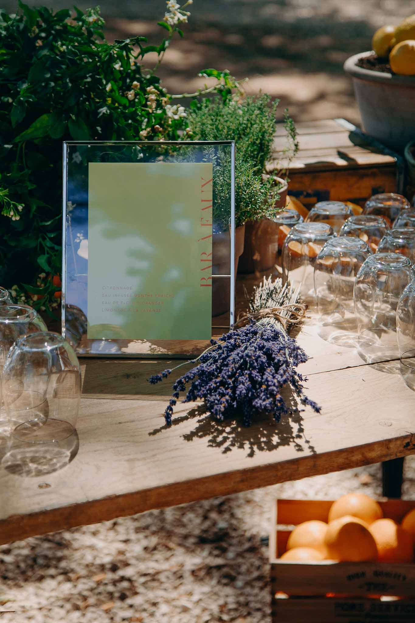 Provencal-styled Bar a Eau drinks station with lavender, citrus, potted herbs, and a framed sage green menu sign