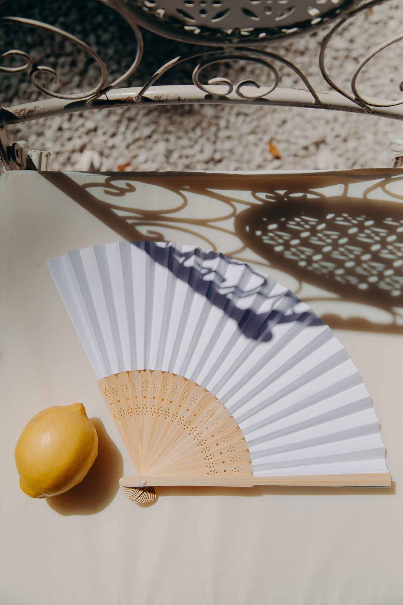 White striped paper hand fan with bamboo handle and lemon styled as wedding favour in natural sunlight