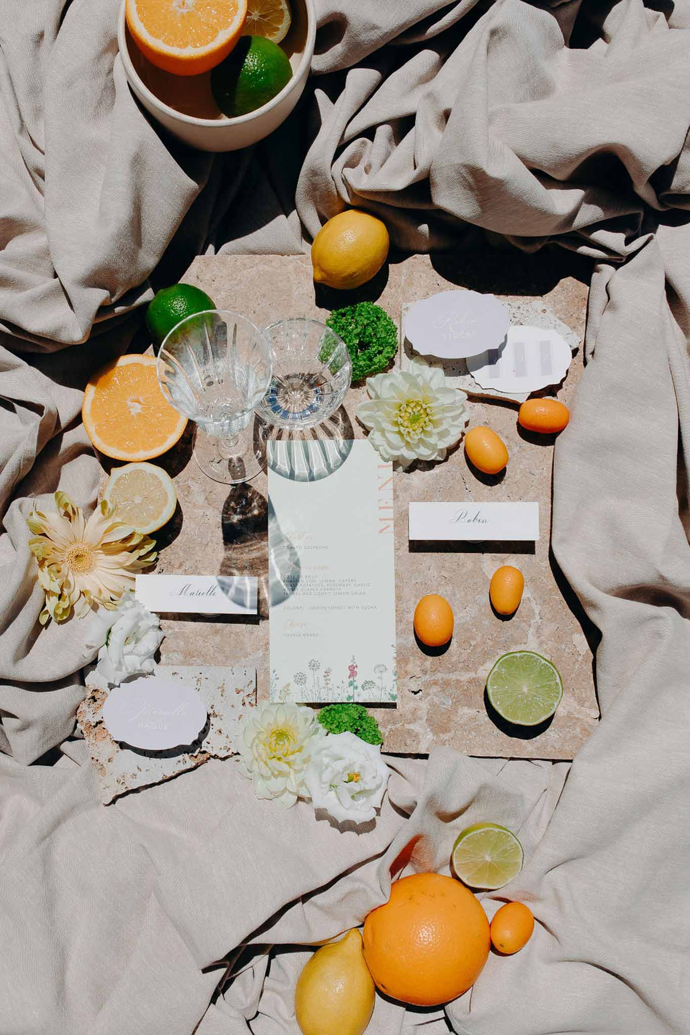 Flat lay of mint green menu card with botanical illustrations, place cards, crystal glasses, and citrus fruits