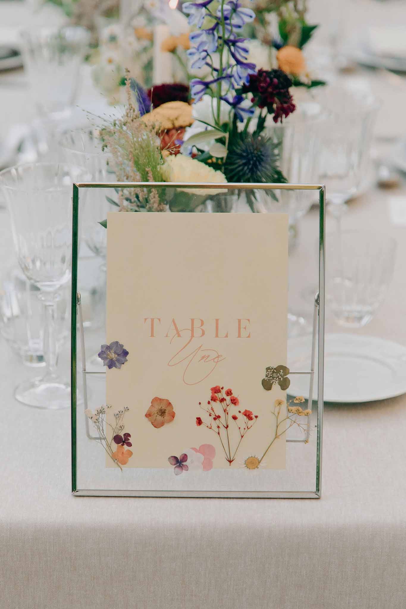 Table Un number card with botanical illustration beside wildflower centrepiece of delphiniums and scabiosa