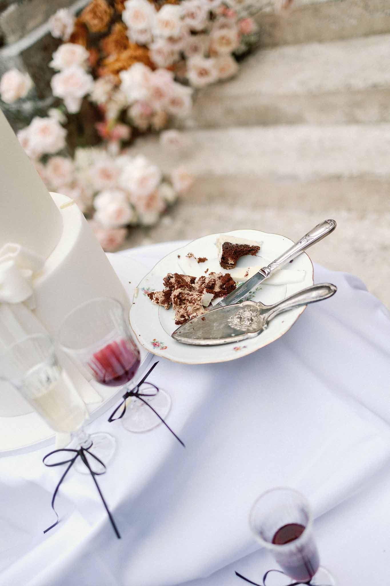 Cake cutting setup with chocolate cake slices on vintage china, silver server, and red wine glasses
