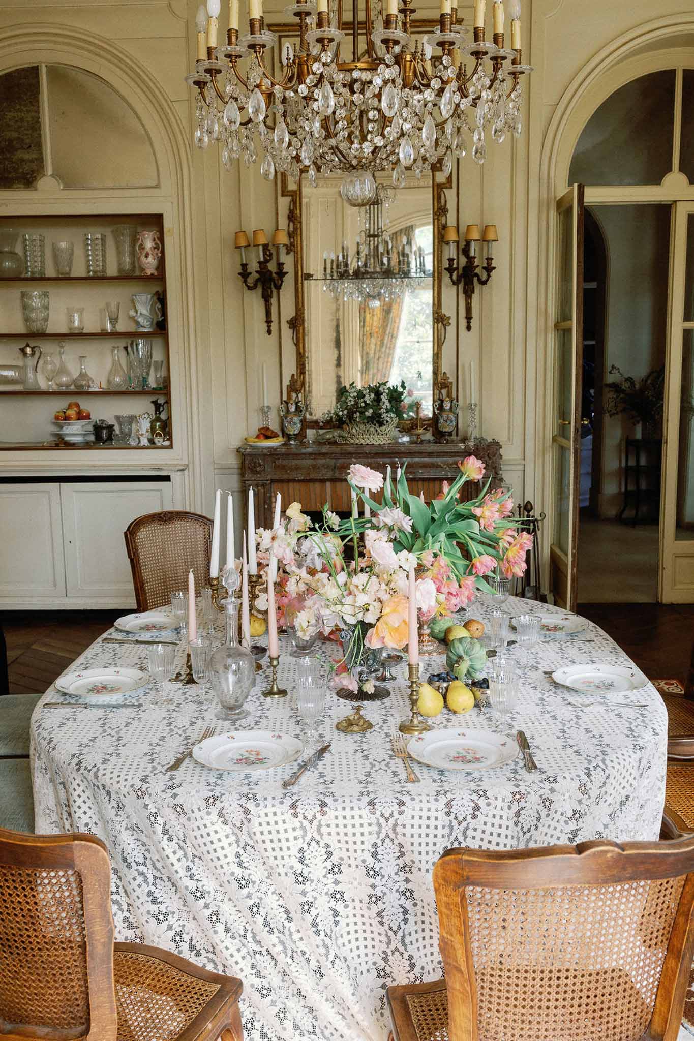 Chateau dining room tablescape with lace cloth, floral porcelain, peach tulips and pink sweet peas, brass candlesticks and...