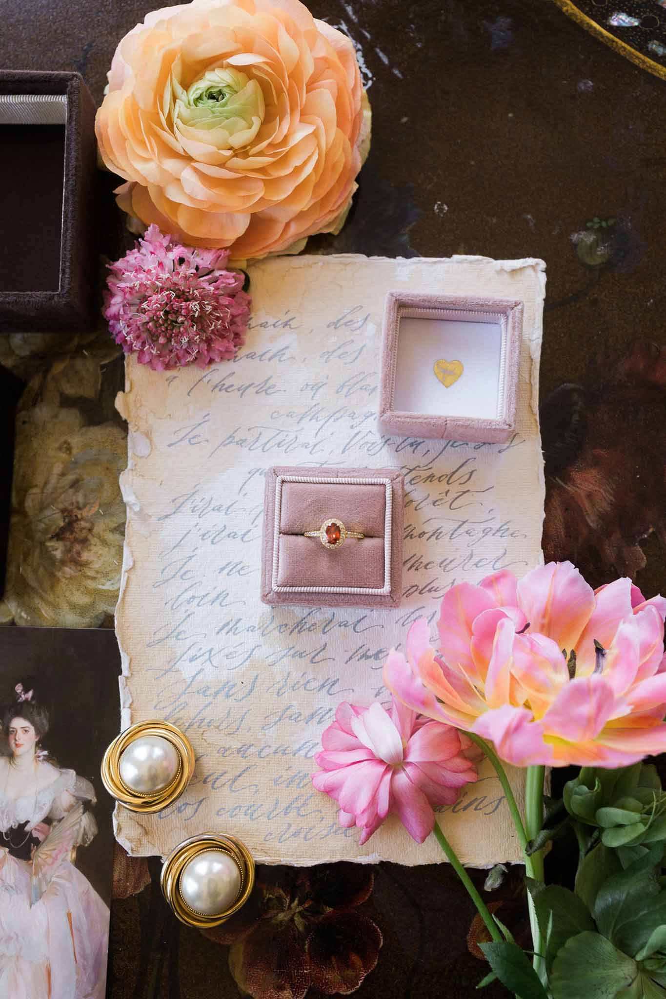Oval gemstone ring in mauve velvet box with gold pearl earrings and parrot tulips on French script