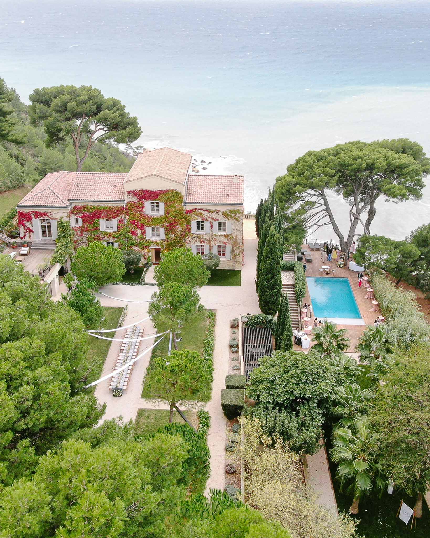Aerial view of coastal villa with reception table pool deck and turquoise sea beyond