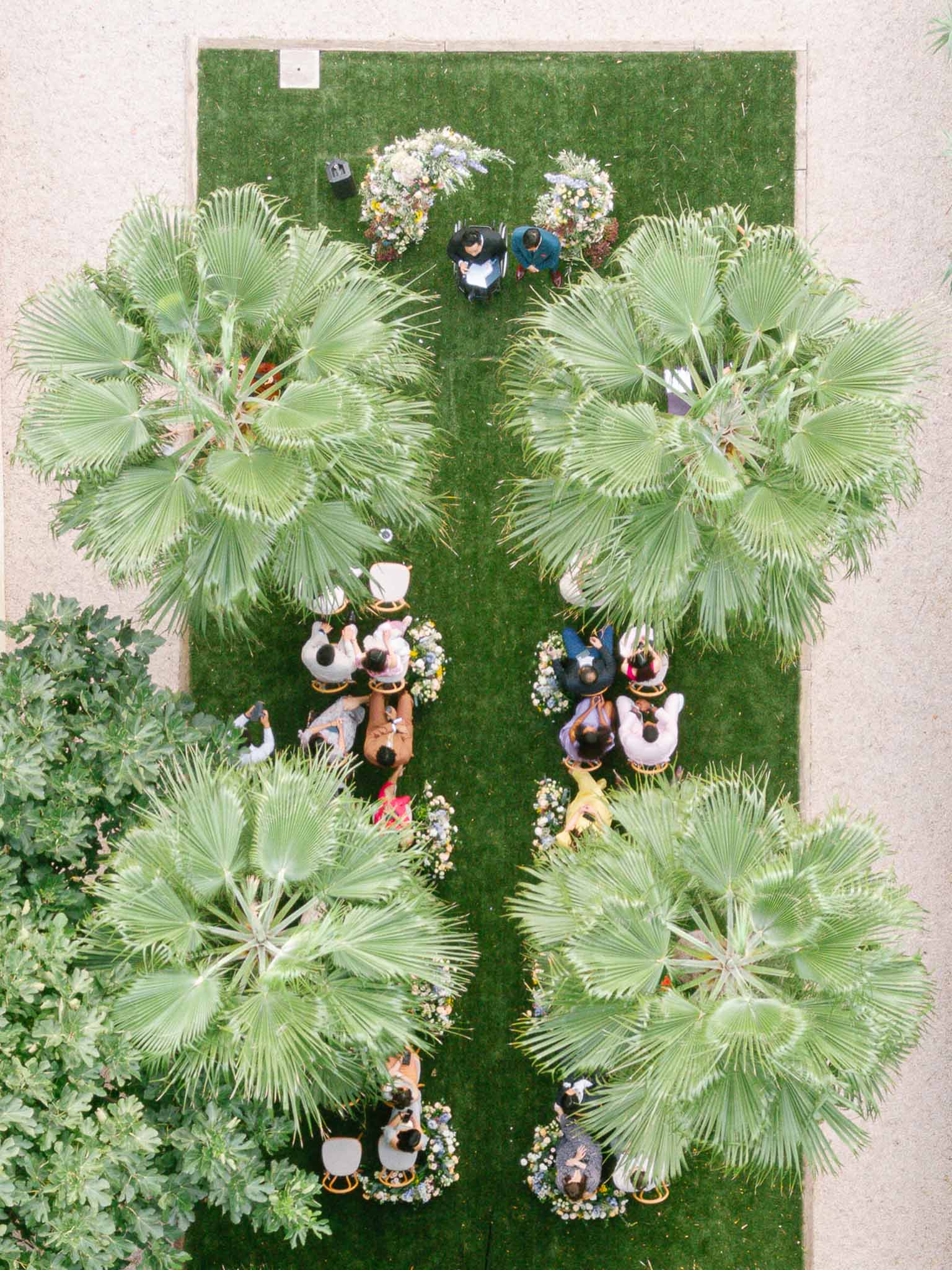 Aerial view of outdoor ceremony on lawn with fan palms, white and blue floral arrangements, and seated guests