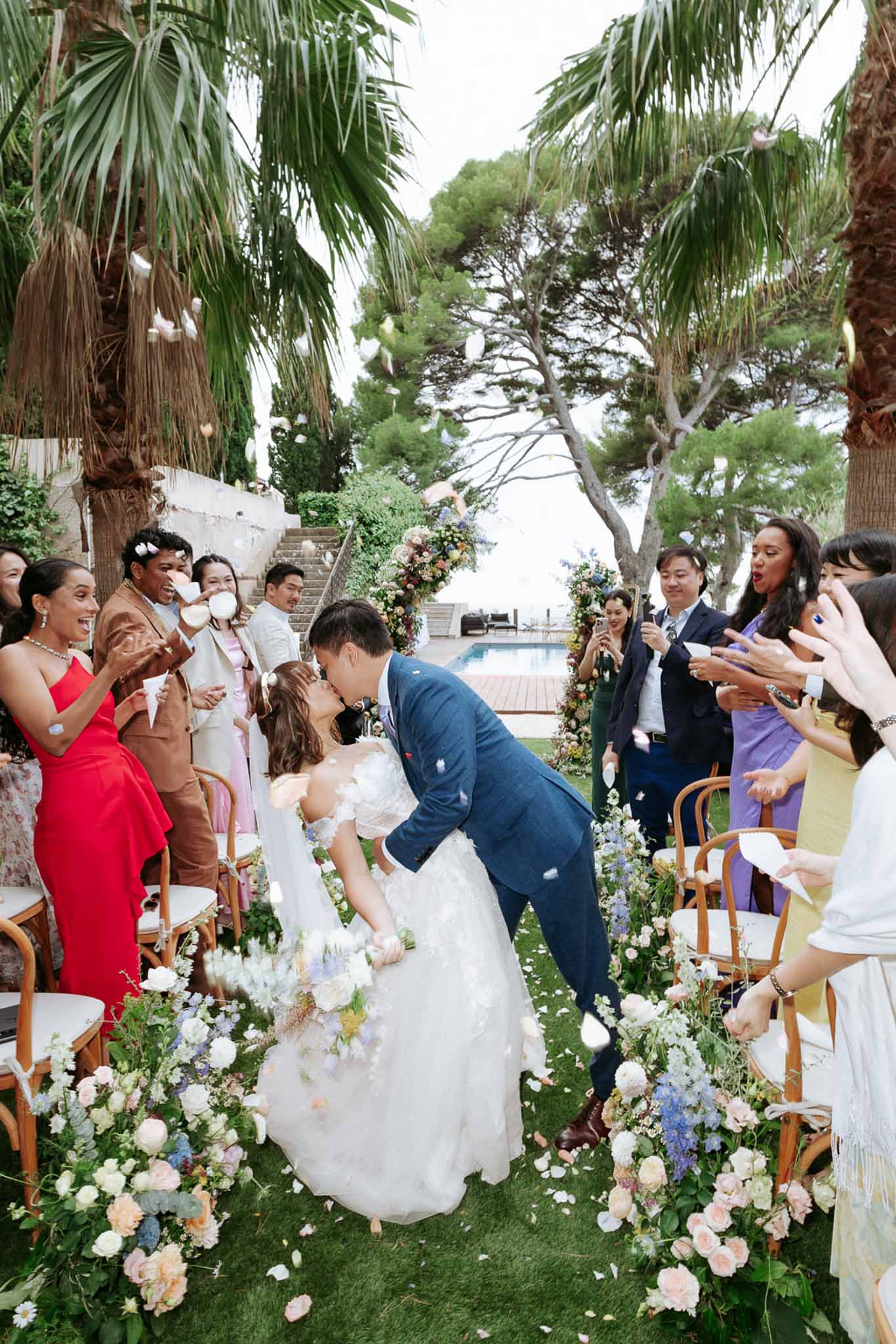 Dip kiss recessional with petal toss past peach rose and blue delphinium aisle arrangements at villa