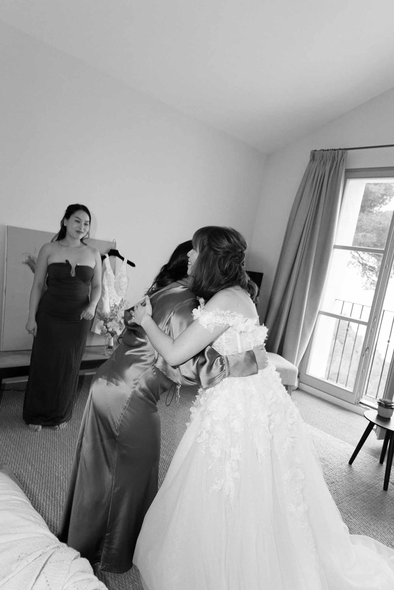 Bride in off-the-shoulder lace ball gown embracing bridesmaid in satin dress in black and white