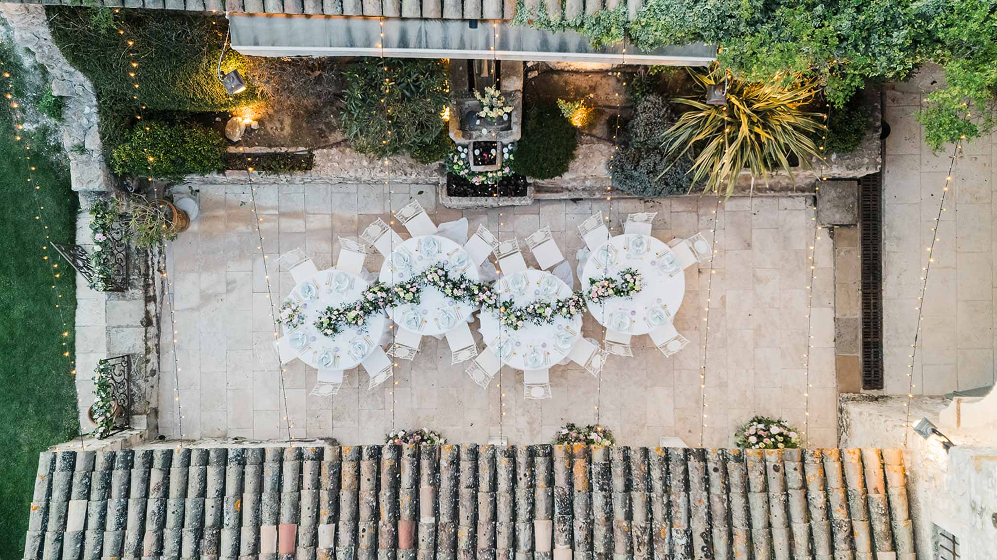 Aerial view of outdoor cocktail reception with round tables and floral centerpieces in stone courtyard