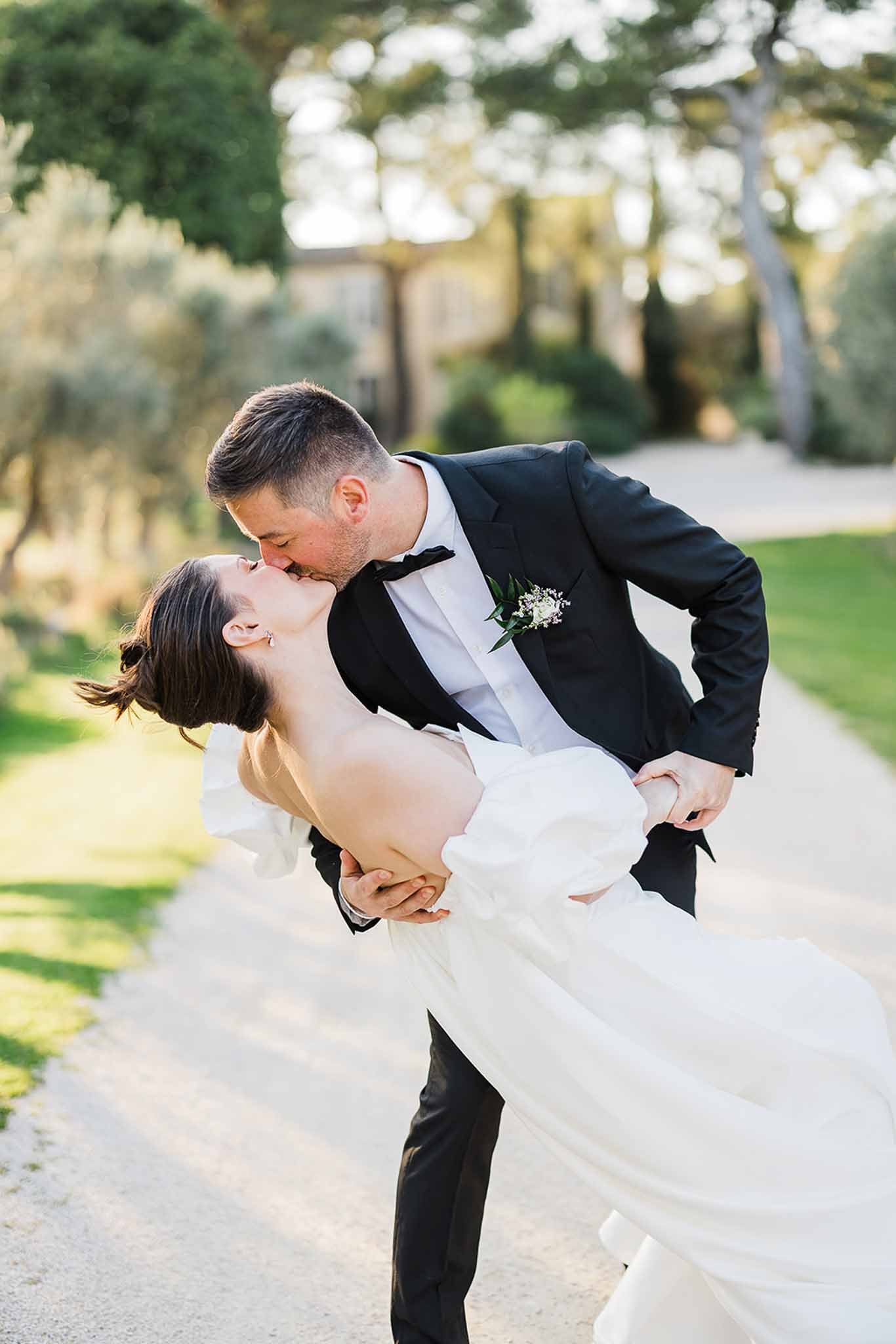 Groom lifting and kissing bride in romantic portrait on stone pathway in garden courtyard setting