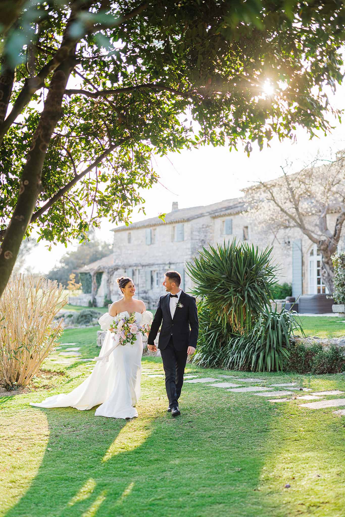 Bride and groom walking through manicured gardens at stone villa wedding venue