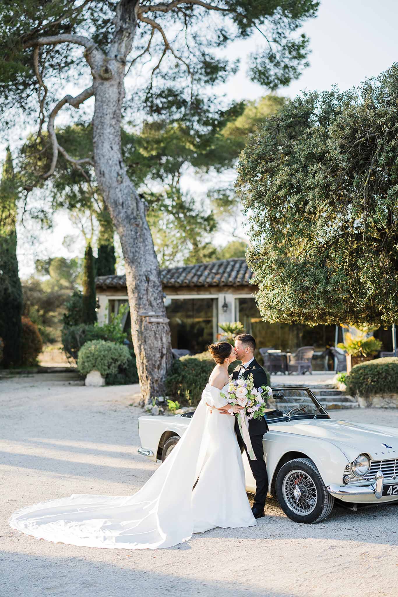 Bride and groom posing with vintage white convertible at Mediterranean-style courtyard wedding venue