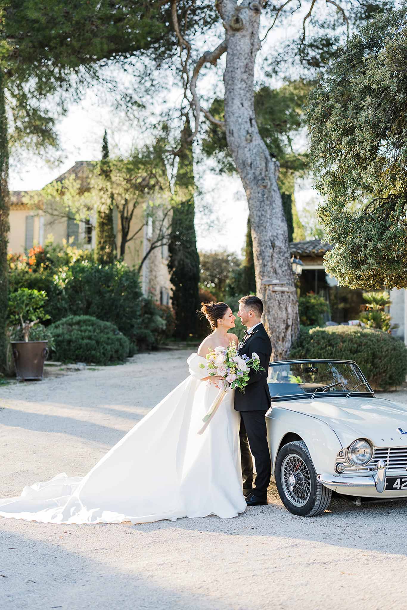 Bride and groom pose with vintage car in Mediterranean garden courtyard