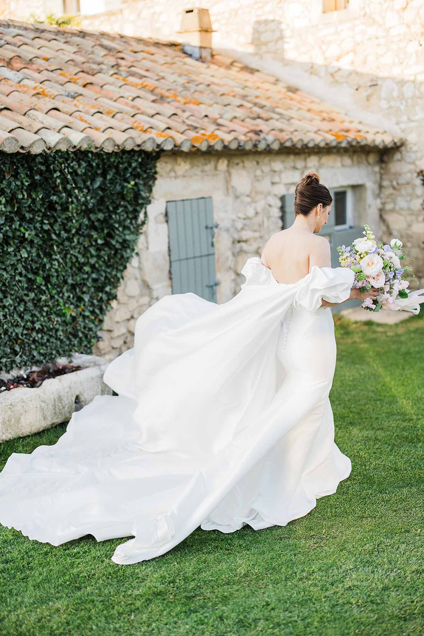 Bride in ivory gown with blush bouquet beside ivy-covered stone cottage