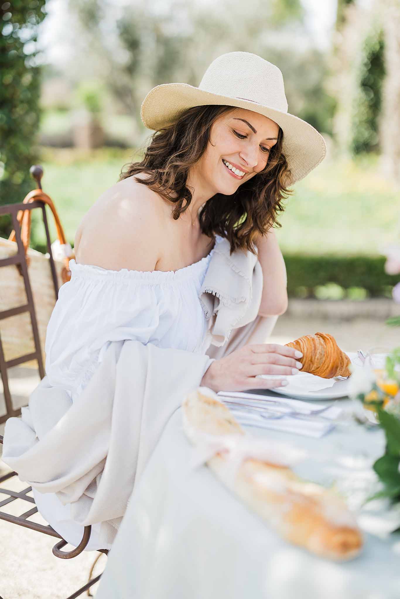 Bride in white dress and cowboy hat enjoying breakfast at garden table with pastries