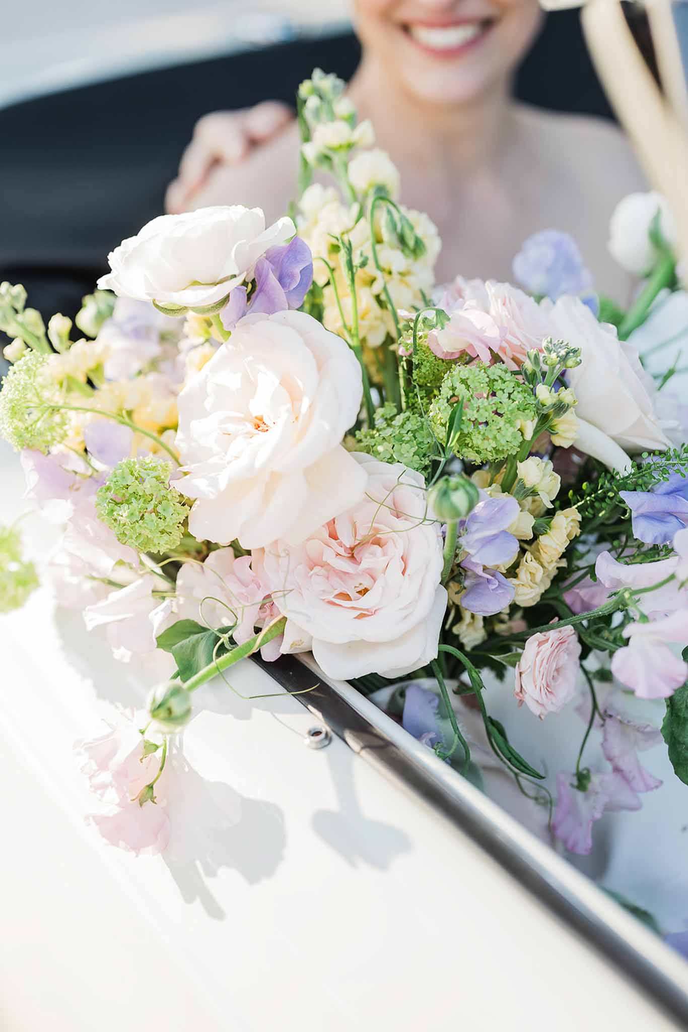 Bride holding garden-style bouquet with roses and sweet peas at outdoor wedding