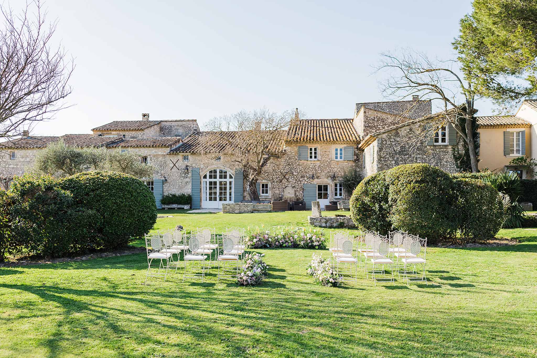 Outdoor wedding ceremony setup on lawn at stone manor house with white chairs and floral arrangements