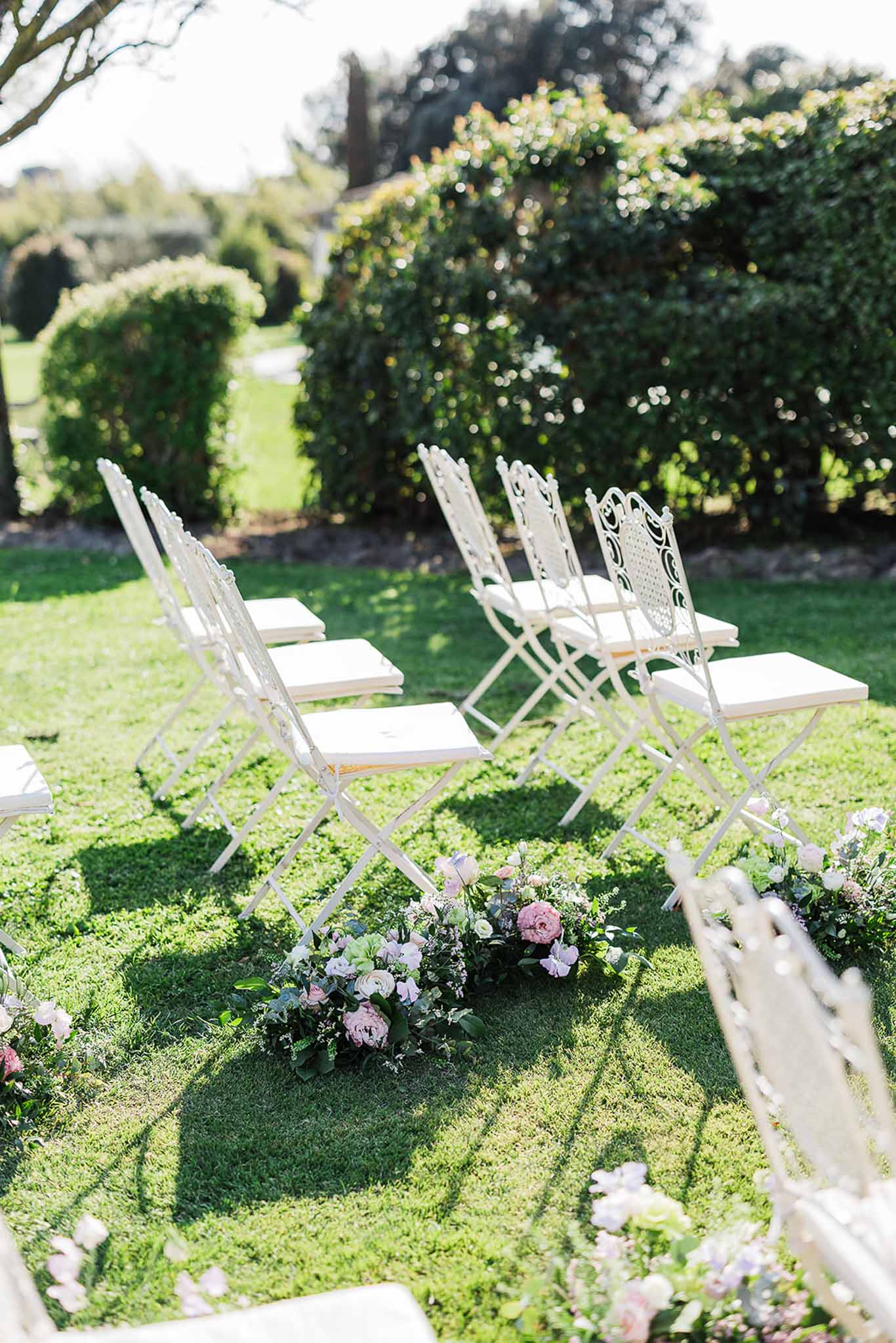 Outdoor wedding ceremony setup with white chairs and pink floral arrangements in formal garden