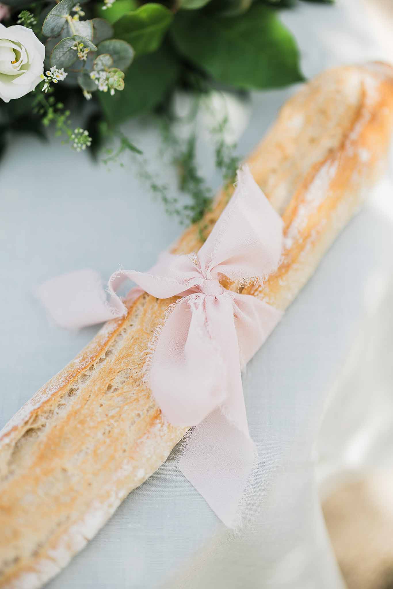 Wedding cake detail with pink ribbon and white rose topper at elegant reception