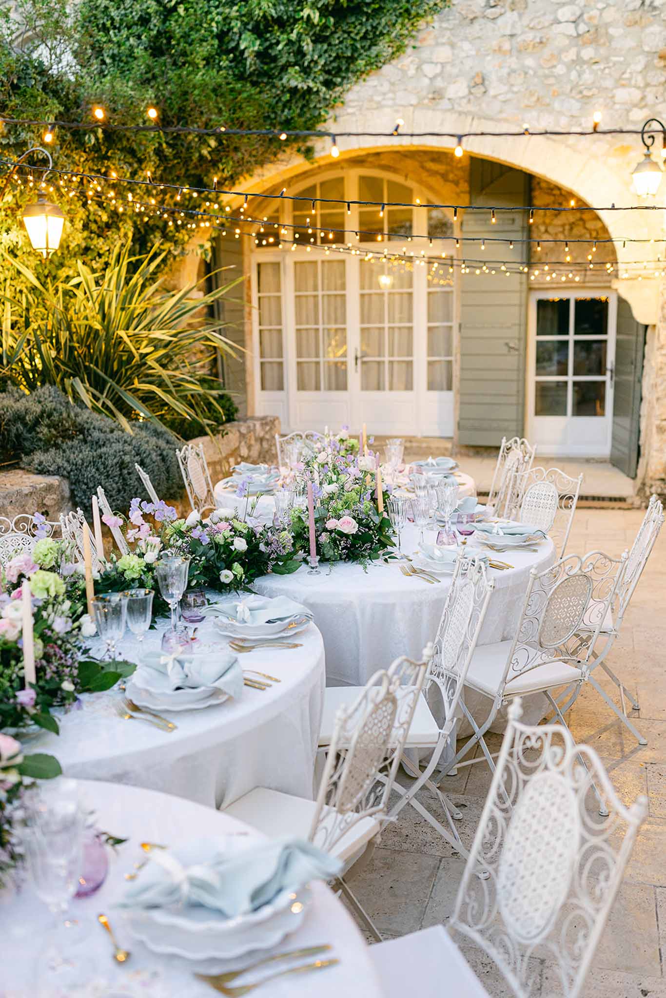 Outdoor reception dinner setup with round tables in stone villa courtyard with string lights