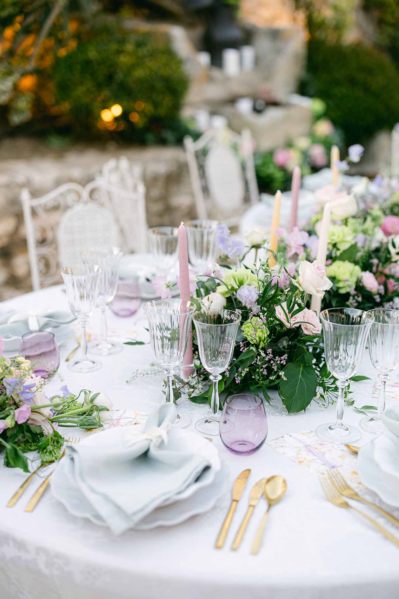 Elegant outdoor reception table setting with pastel florals and gold flatware in stone courtyard