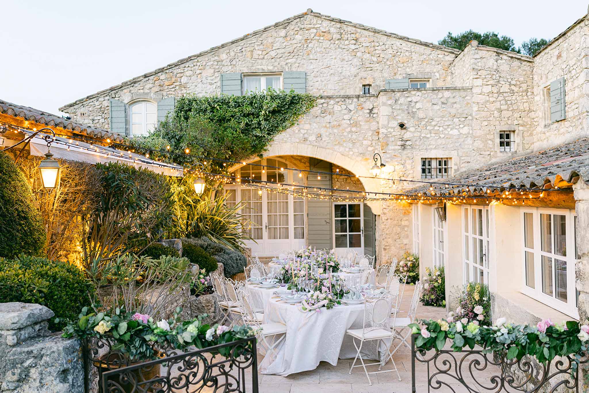 Outdoor reception setup in historic French stone courtyard with ivory linens and lavender centerpieces